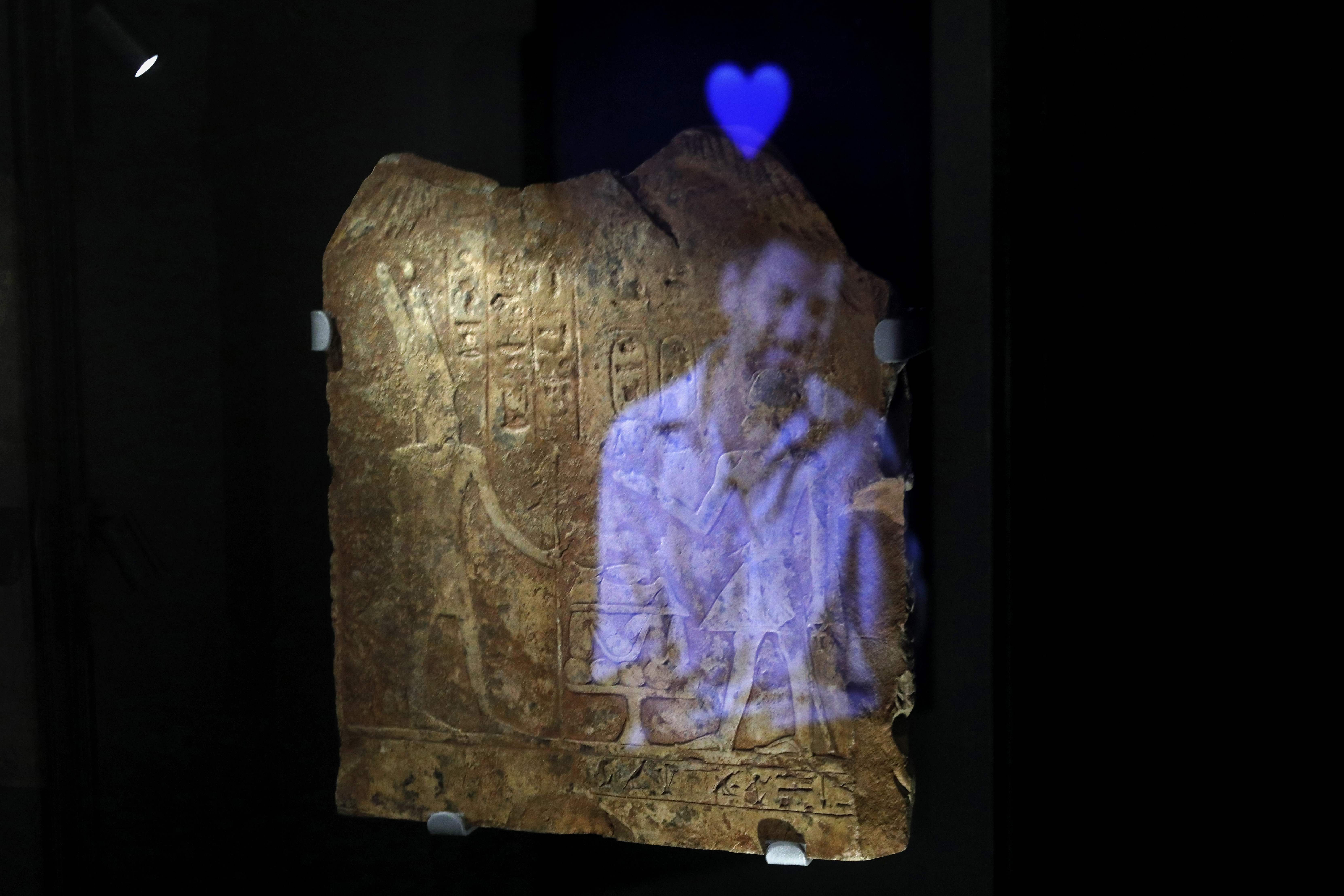 Una instalación de vídeo muestra la imagen de un hombre con el emoji de un corazón azul reflejado en una placa egipcia antigua grabada con jeroglíficos, parte del concepto de esta exposición en Israel.  (Foto Prensa Libre: AFP)