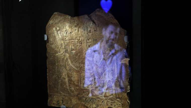Una instalación de vídeo muestra la imagen de un hombre con el emoji de un corazón azul reflejado en una placa egipcia antigua grabada con jeroglíficos, parte del concepto de esta exposición en Israel.  (Foto Prensa Libre:  MENAHEM KAHANA / AFP)