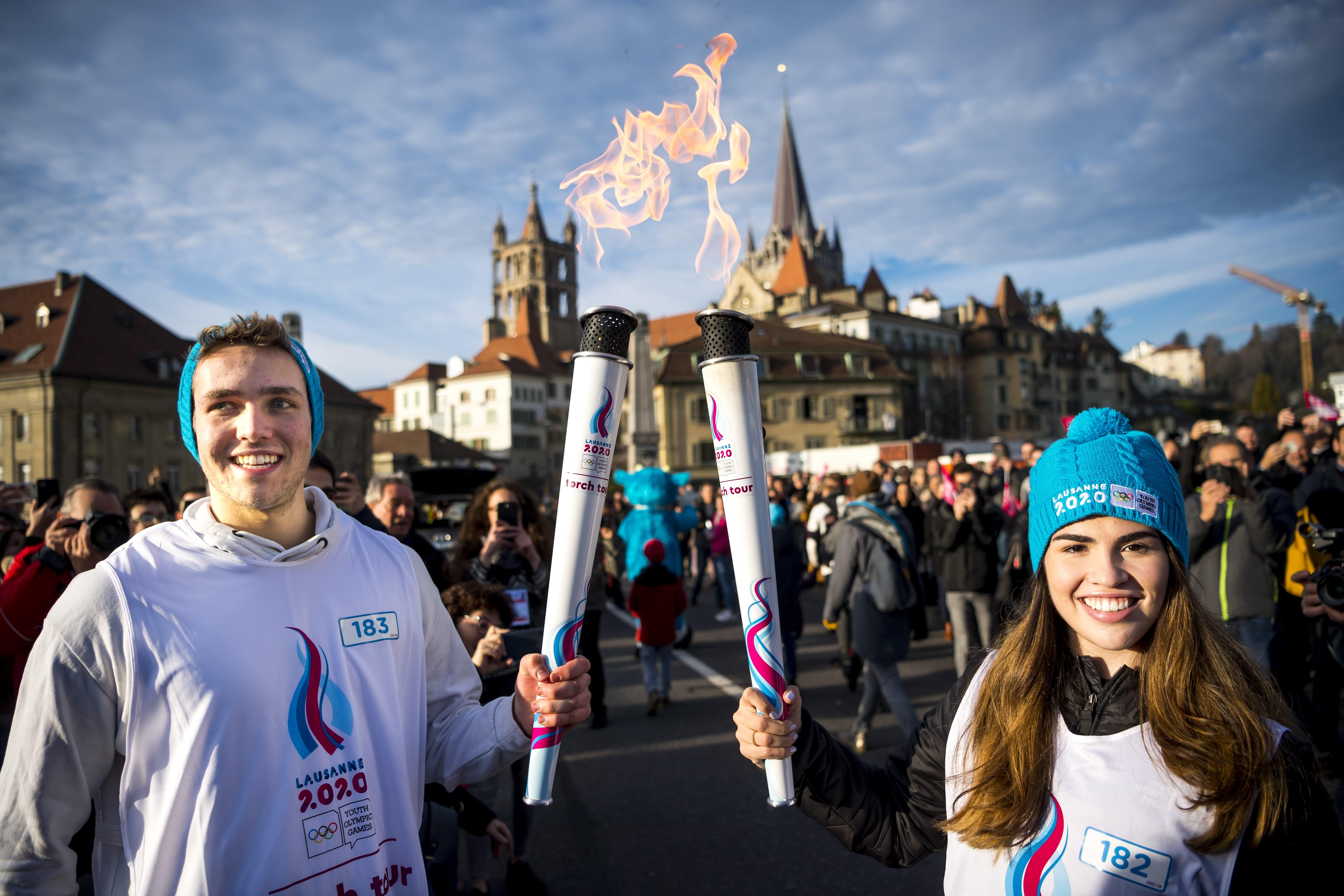 Los jóvenes atletas sostienen la Llama Olímpica de los Juegos Olímpicos de la Juventud de Invierno de Lausana 2020 frente a la catedral de Lausana, Suiza. (Foto Prensa Libre: EFE)