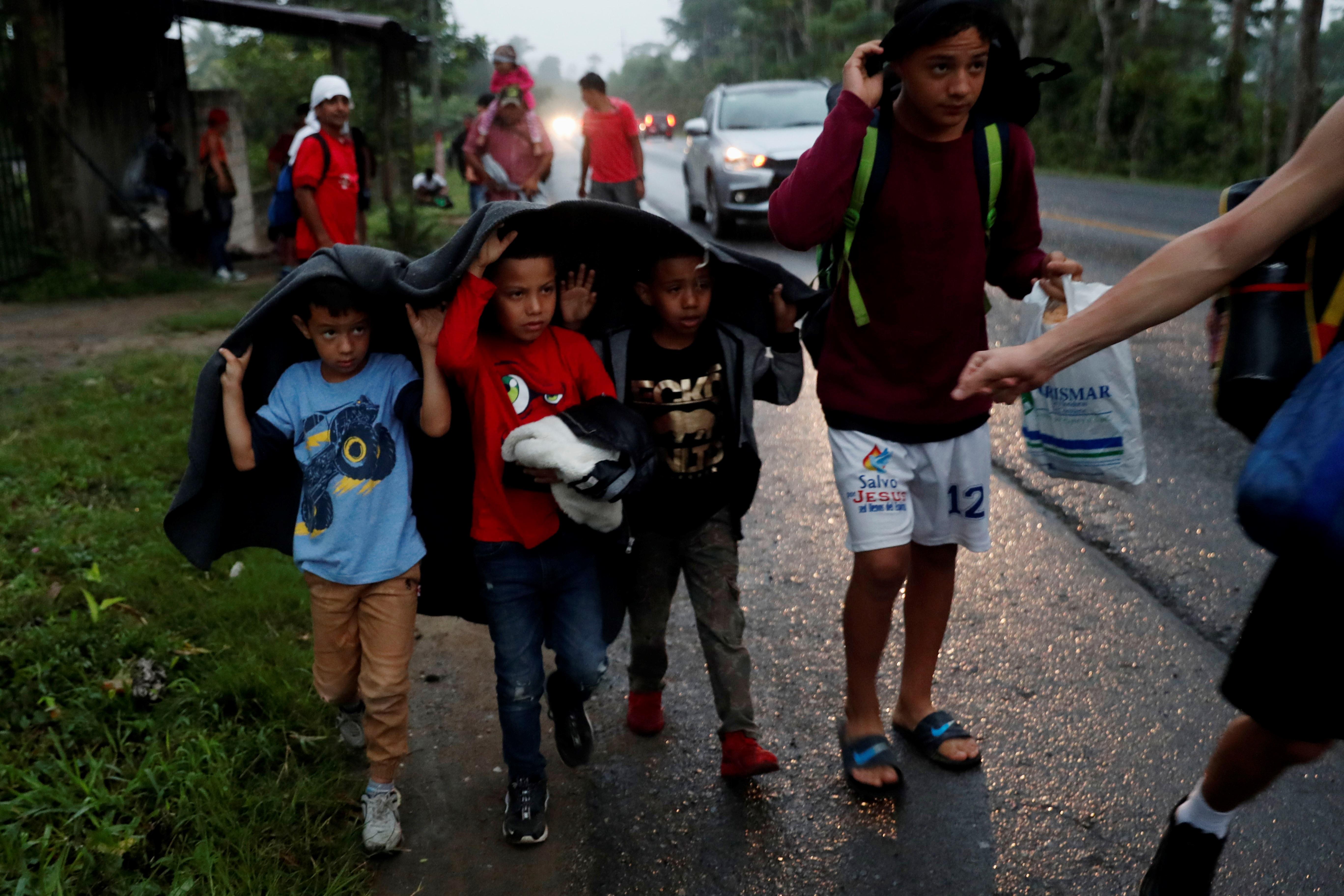 Un grupo de niños que hace parte de la caravana de migrantes hondureños se cubre de la lluvia mientras recorrían una carretera en Chiquimula. (Foto Prensa Libre: EFE)