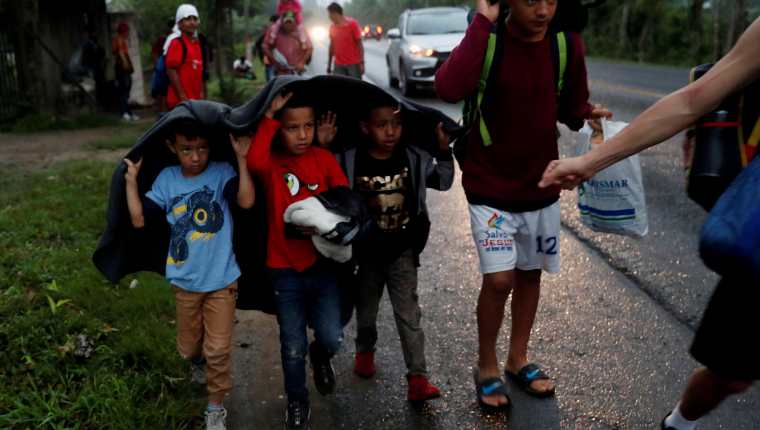 Un grupo de niños que hace parte de la caravana de migrantes hondureños se cubre de la lluvia mientras recorrían una carretera en Chiquimula. (Foto Prensa Libre: EFE)