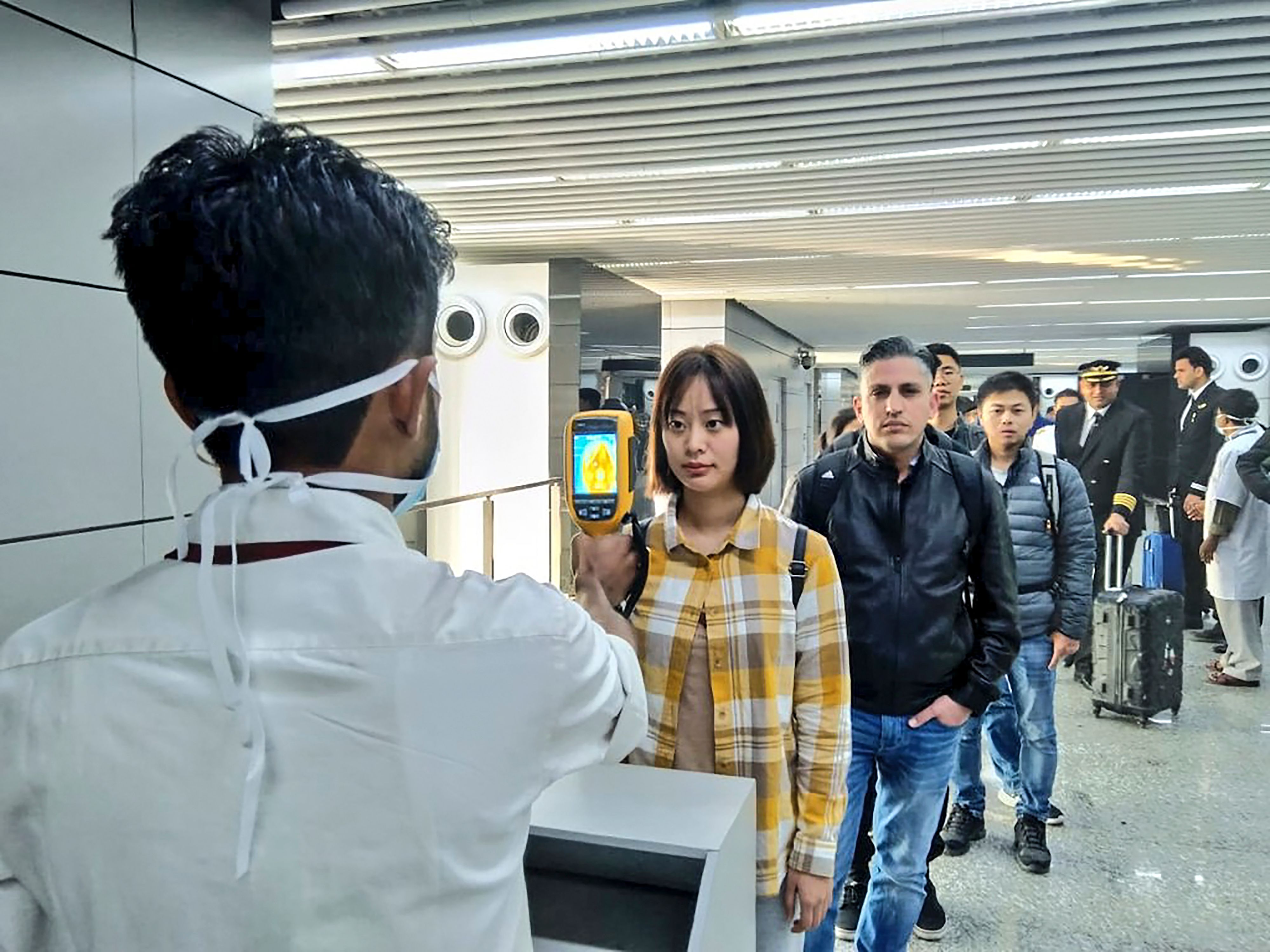 In this handout photograph taken and released by the Ministry of Civil Aviation (MoCA) on January 21, 2020, a man (L) uses a thermographic camera to screen the head of people at Netaji Subhash Chandra Bose International Airport in Kolkata, following the Ministry of Health and Family Welfare's advisory to screen passengers arriving in India from China and Hong Kong regarding the novel coronavirus (nCoV) issue. - Asian countries on January 21 ramped up measures to block the spread of a new virus as the death toll in China rose to six and the number of cases jumped to almost 300, raising concerns in the middle of a major holiday travel rush. (Photo by Handout / Ministry of Civil Aviation (MoCA) / AFP) / RESTRICTED TO EDITORIAL USE - MANDATORY CREDIT "AFP PHOTO / Ministry of Civil Aviation (MoCA)" - NO MARKETING - NO ADVERTISING CAMPAIGNS - DISTRIBUTED AS A SERVICE TO CLIENTS