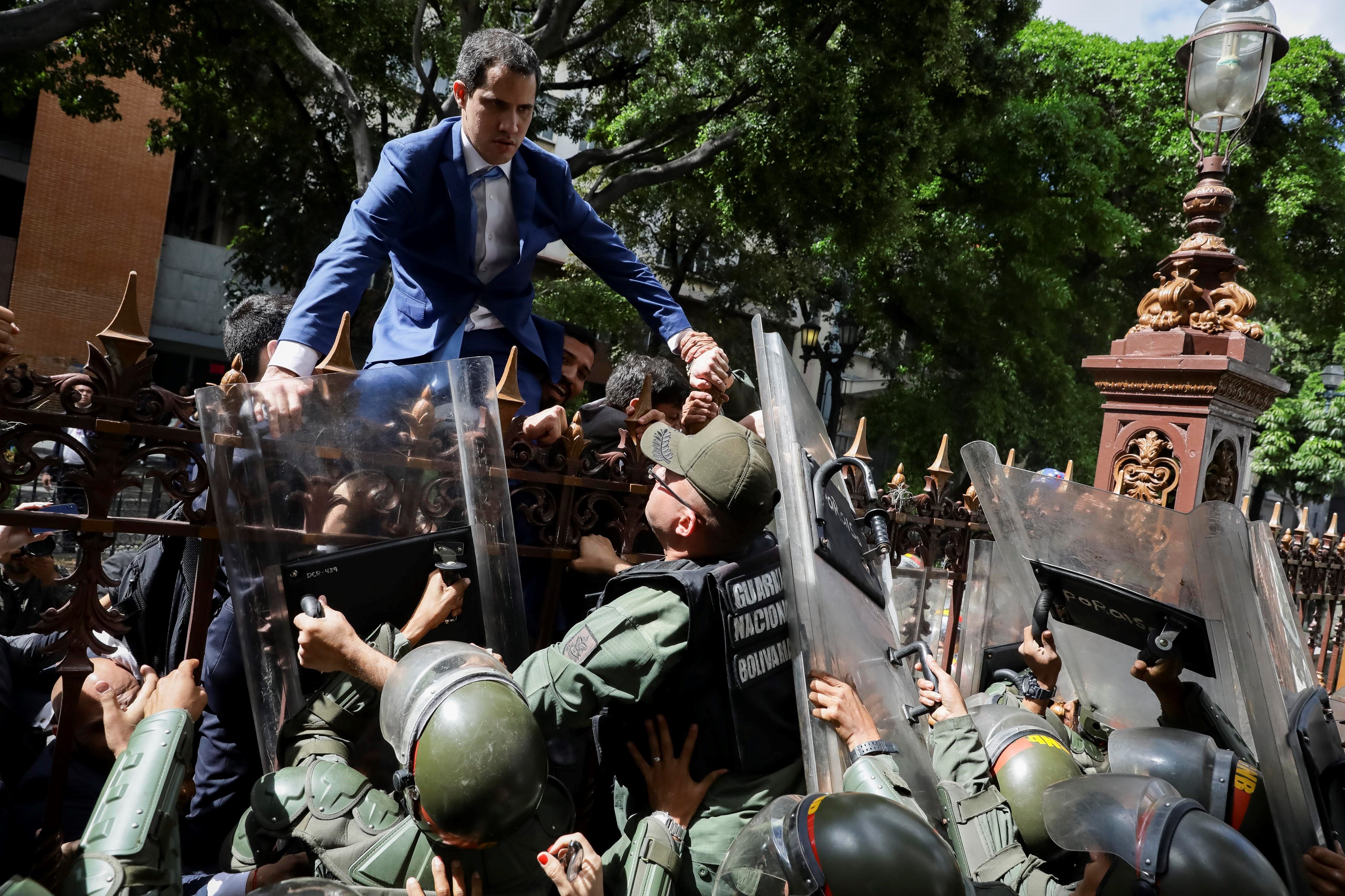 El líder opositor Juan Guaidó trepa una reja en un intento por ingresar a la sede de la Asamblea Nacional, custodiada por la policía para impedir su ingreso. (Foto Prensa Libre: EFE)