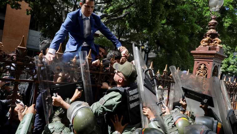 El líder opositor Juan Guaidó trepa una reja en un intento por ingresar a la sede de la Asamblea Nacional, custodiada por la policía para impedir su ingreso. (Foto Prensa Libre: EFE)