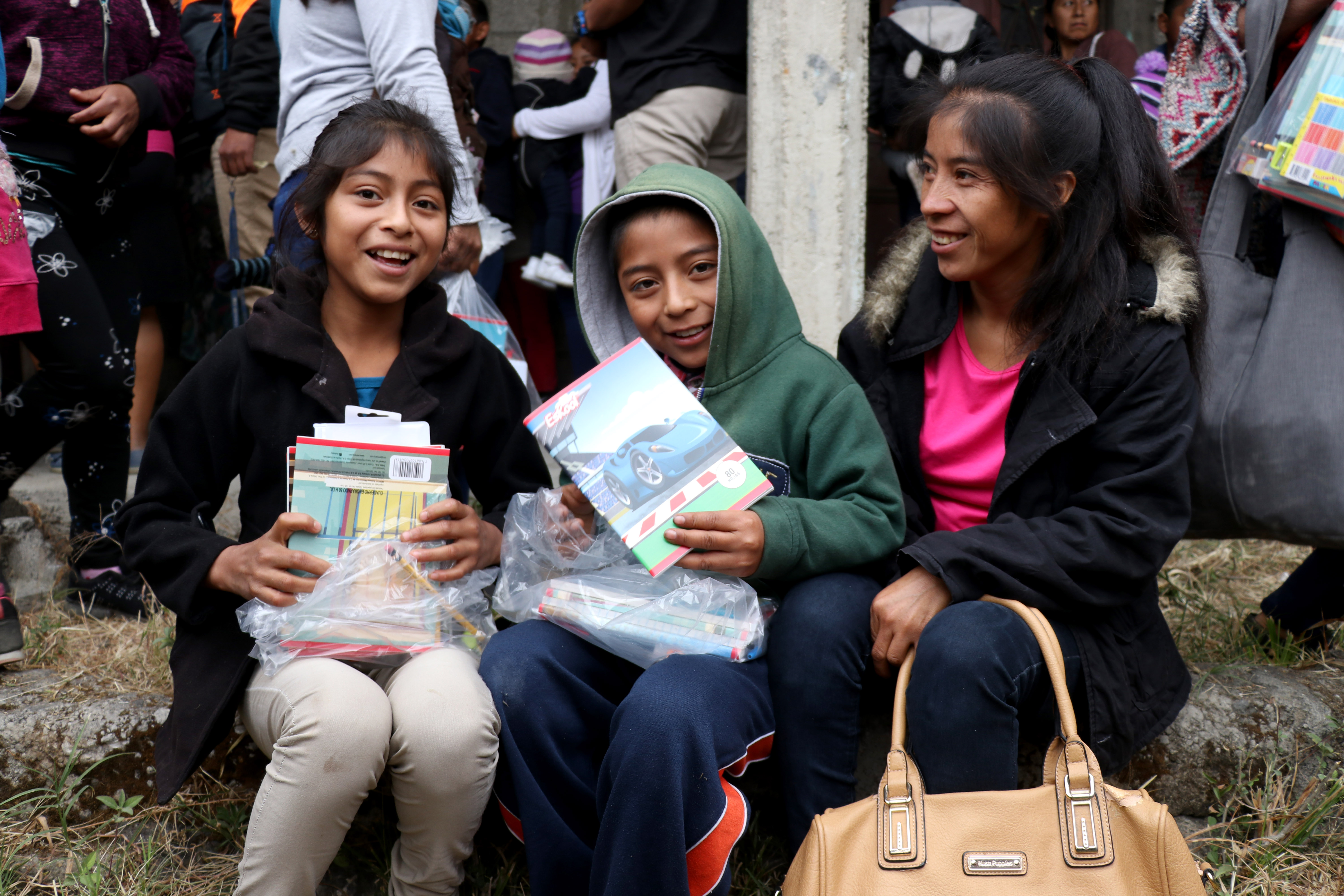 Dos niños junto a su madre sonríen luego de recibir una bolsa con útiles escolares donados por familiares del veterano de guerra, Domingo Tomás. (Foto Prensa Libre. Mike Castillo)