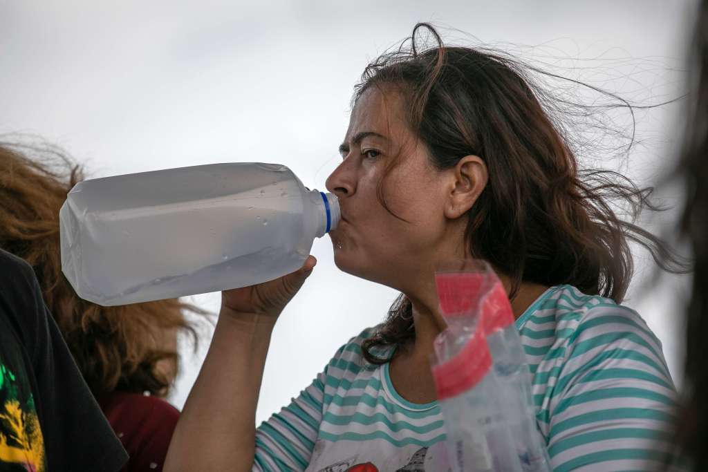 Una mujer agotada debido a las altas temperaturas bebe agua mientras espera en un centro de procesamiento de la Patrulla Fronteriza de los EE.UU.