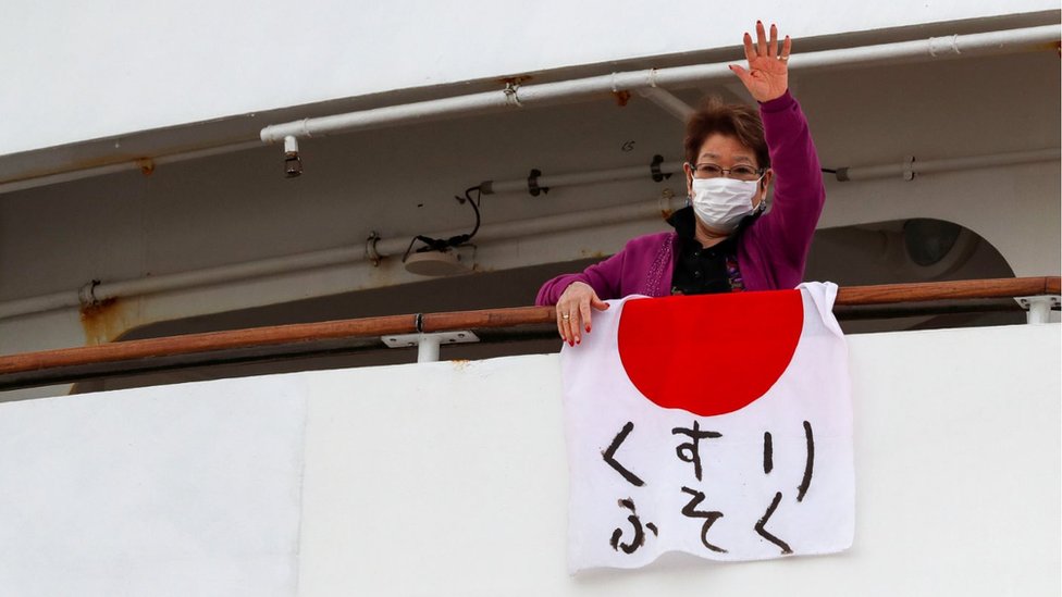 Una pasajera del crucero Dream Princess exhibe una bandera japonesa en la que alerta sobre la falta de medicamentos.