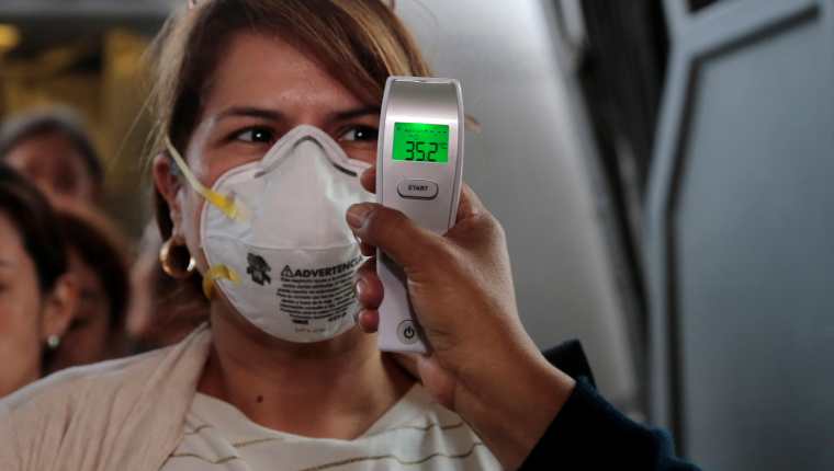 Médicos guatemaltecos toman la temperatura a pasajeros que bajan en el Aeropuerto La Aurora. (Foto Prensa Libre: EFE)
