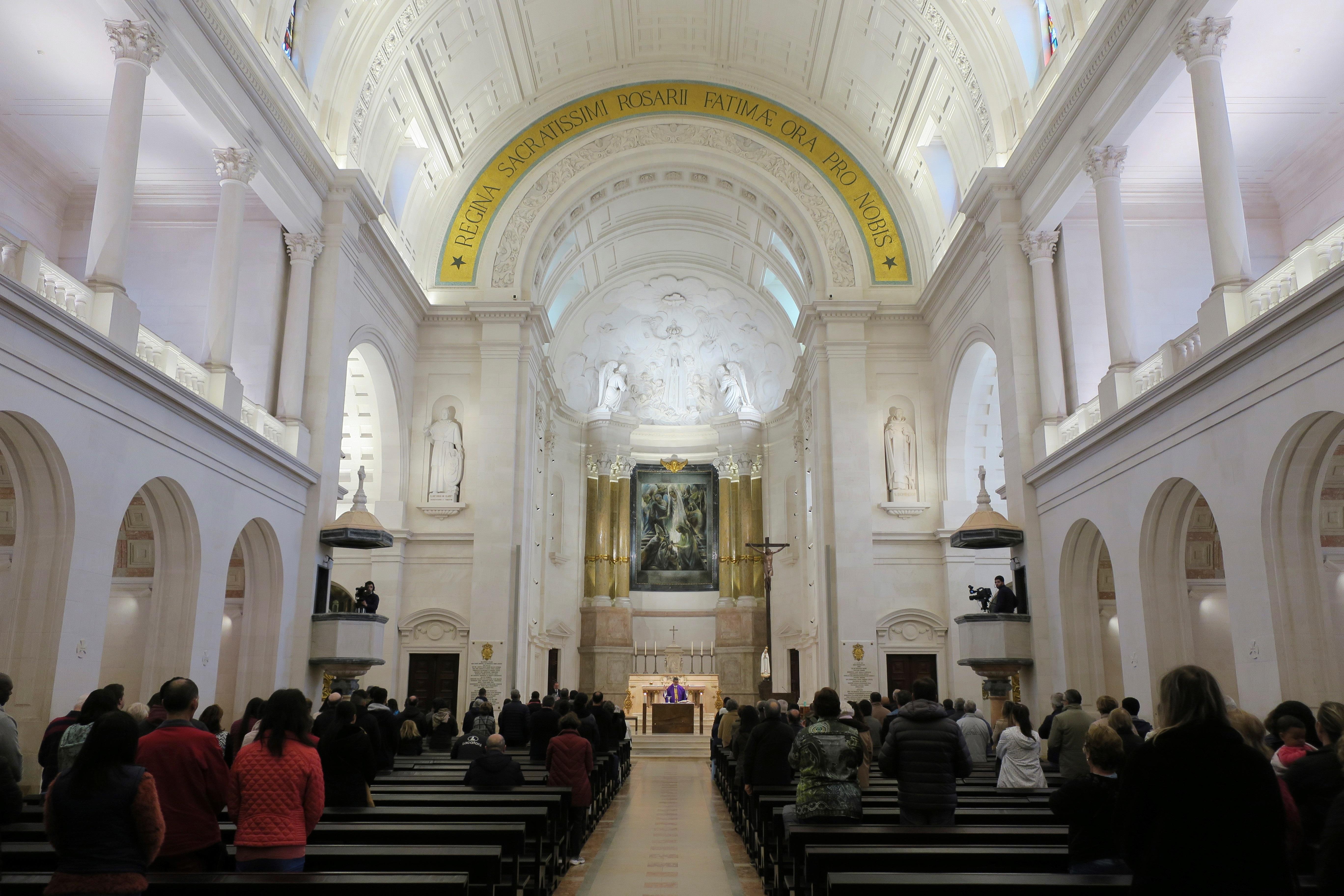 Cientos de fieles se concentran en la basílica del Santuario de Fátima cuando se acerca la hora del ángelus. El culto avanza como cualquier otro día, pero no hay agua bendita, la comunión se entrega en mano y se recomienda evitar los abrazos y el contacto directo con desconocidos. (Foto Prensa Libre: EFE)
