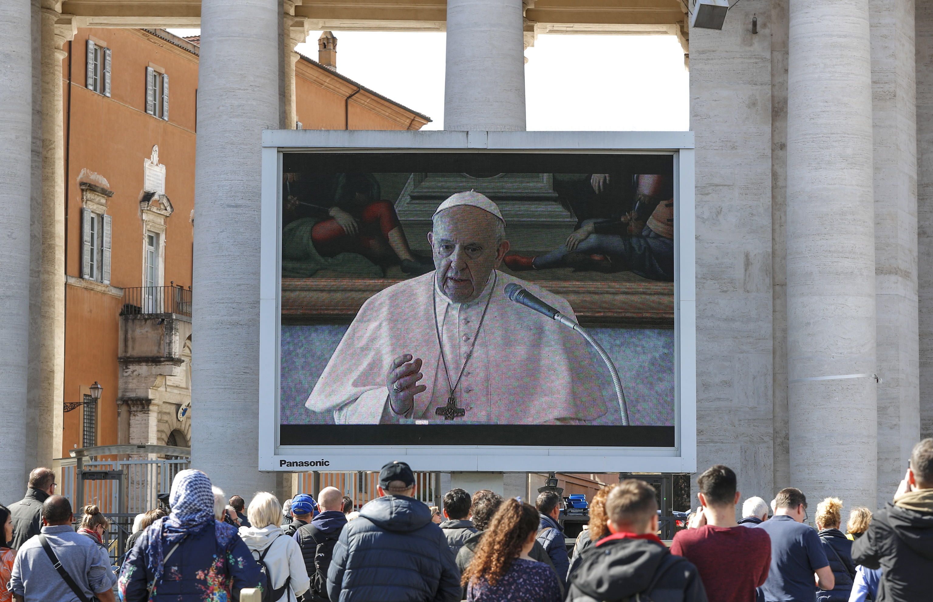 Turistas y fieles católicos con máscaras médicas observan una pantalla gigante instalada en la Plaza de San Pedro, Ciudad del Vaticano. (Foto Prensa Libre: EFE)