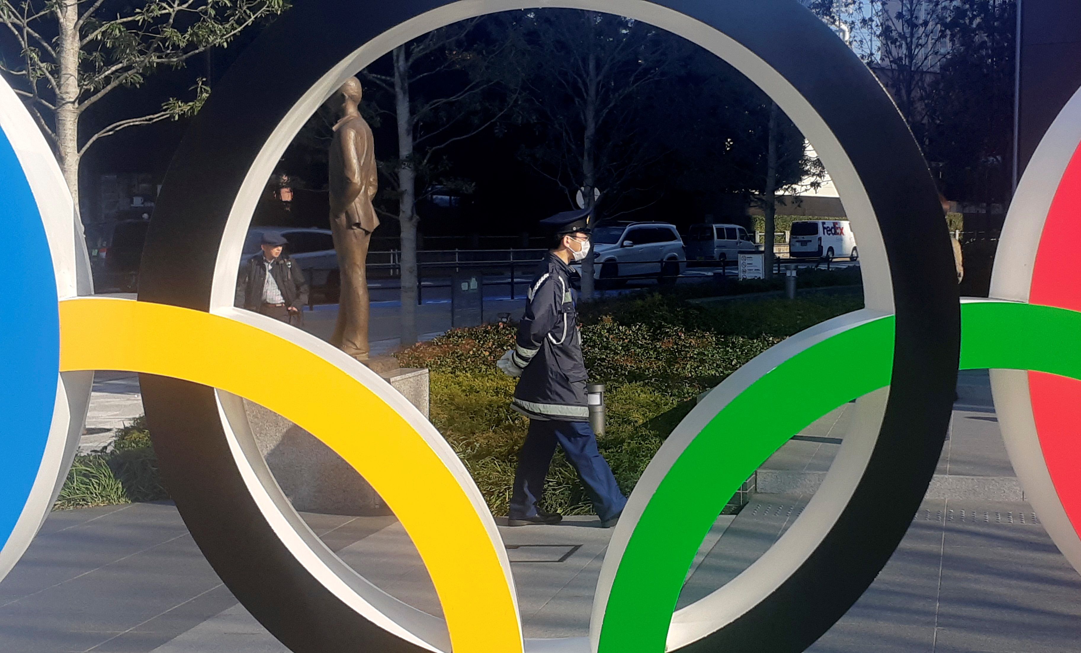  Un policía protegido por una máscara para evitar posibles contagios pasea junto a los anillos olímpicos instalados en Tokio. (Foto Prensa Libre: EFE)