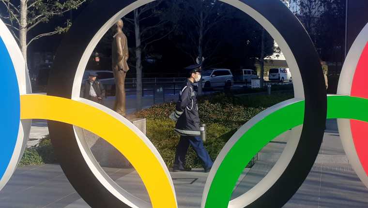  Un policía protegido por una máscara para evitar posibles contagios pasea junto a los anillos olímpicos instalados en Tokio. (Foto Prensa Libre: EFE)