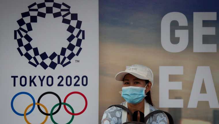 -FOTODELDÍA- ZSN01. BANGKOK (TAILANDIA), 24/03/2020.- Una mujer con una máscara sanitaria aguarda la llegada del autobús frente a un cartel de los Juegos Olímpicos de Tokio 2020 EFE/DIEGO AZUBEL