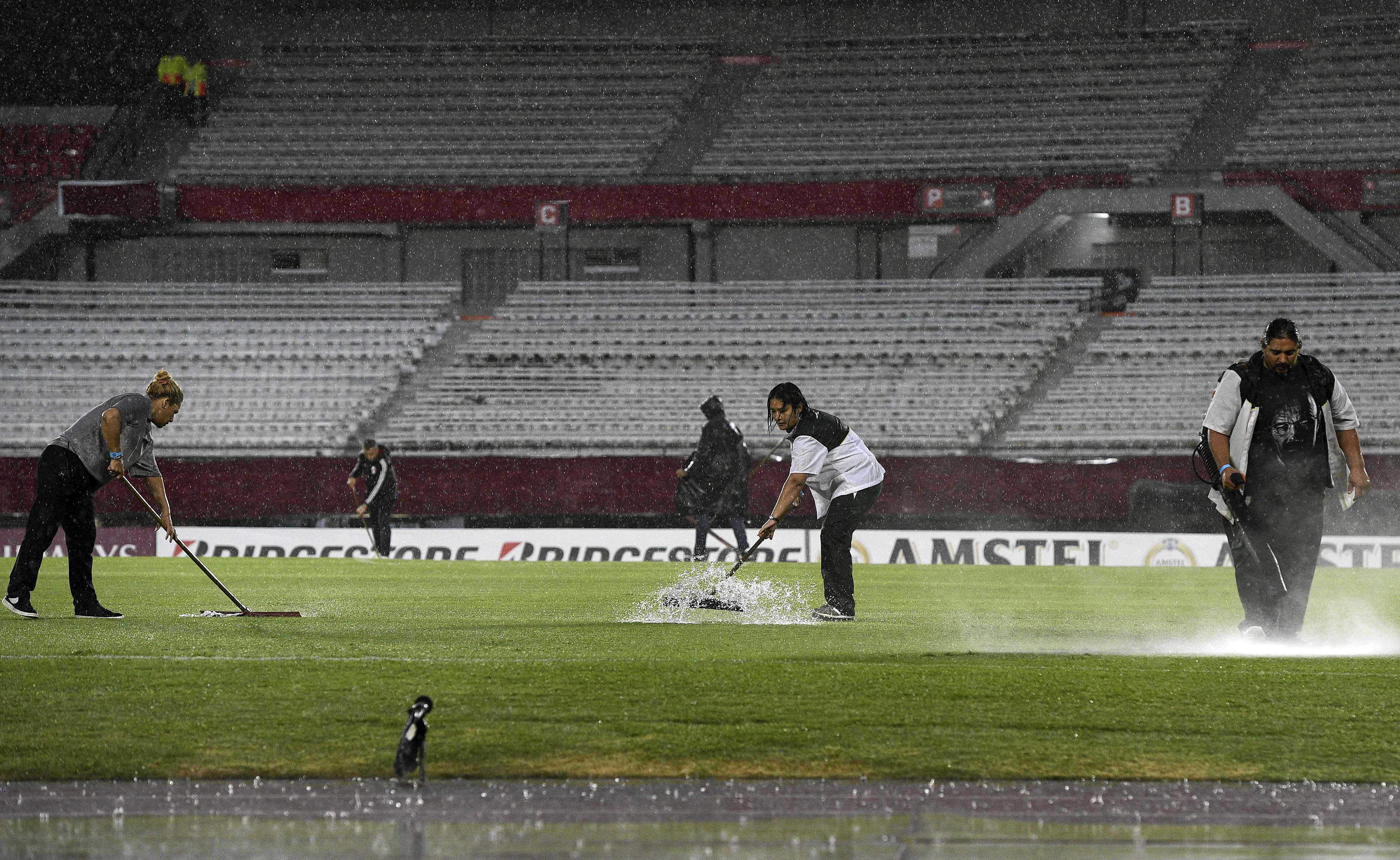 Trabajadores remueven agua ante del juego entre River y Deportivo Binacional en el Estadio Monumental de Buenos Aires. (Foto Prensa Libre: AFP)