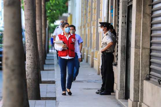 Una colaboraba de la Cruz Roja Guatemalteca camina por la 8va.  Avenida de la zona 1 portando su mascarilla ante la atenta mirada de un agente de la PNC postrado en el ingreso del Congreso de la República. Foto Prensa Libre:  Juan Diego González.