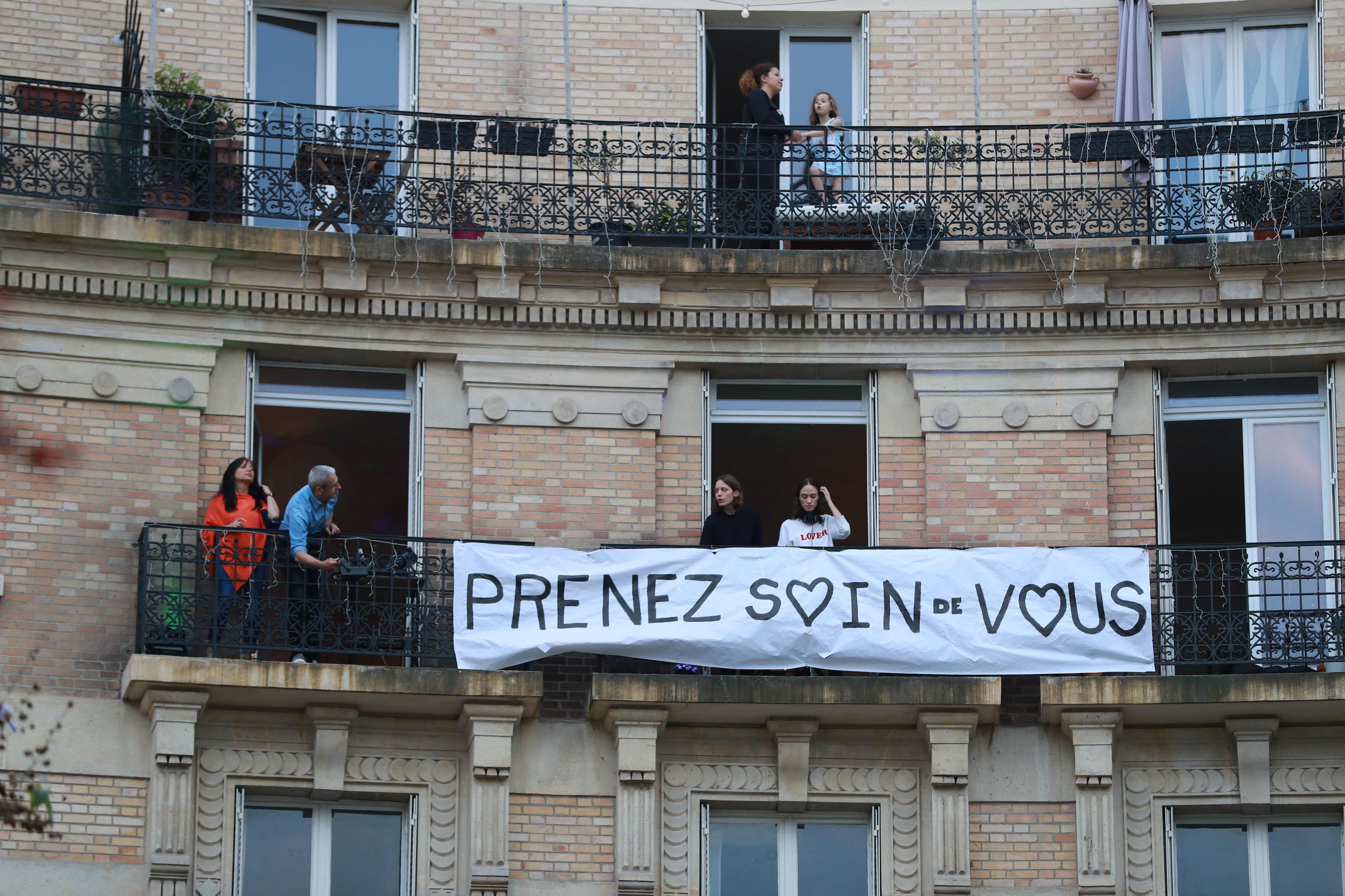 Un grupo de DJ´s  se paran junto a una pancarta que dice 'Cuídate' mientras tocan música en el balcón de su apartamento para las personas del vecindario en solidaridad por el confinamiento. (Foto Prensa Libre: AFP)