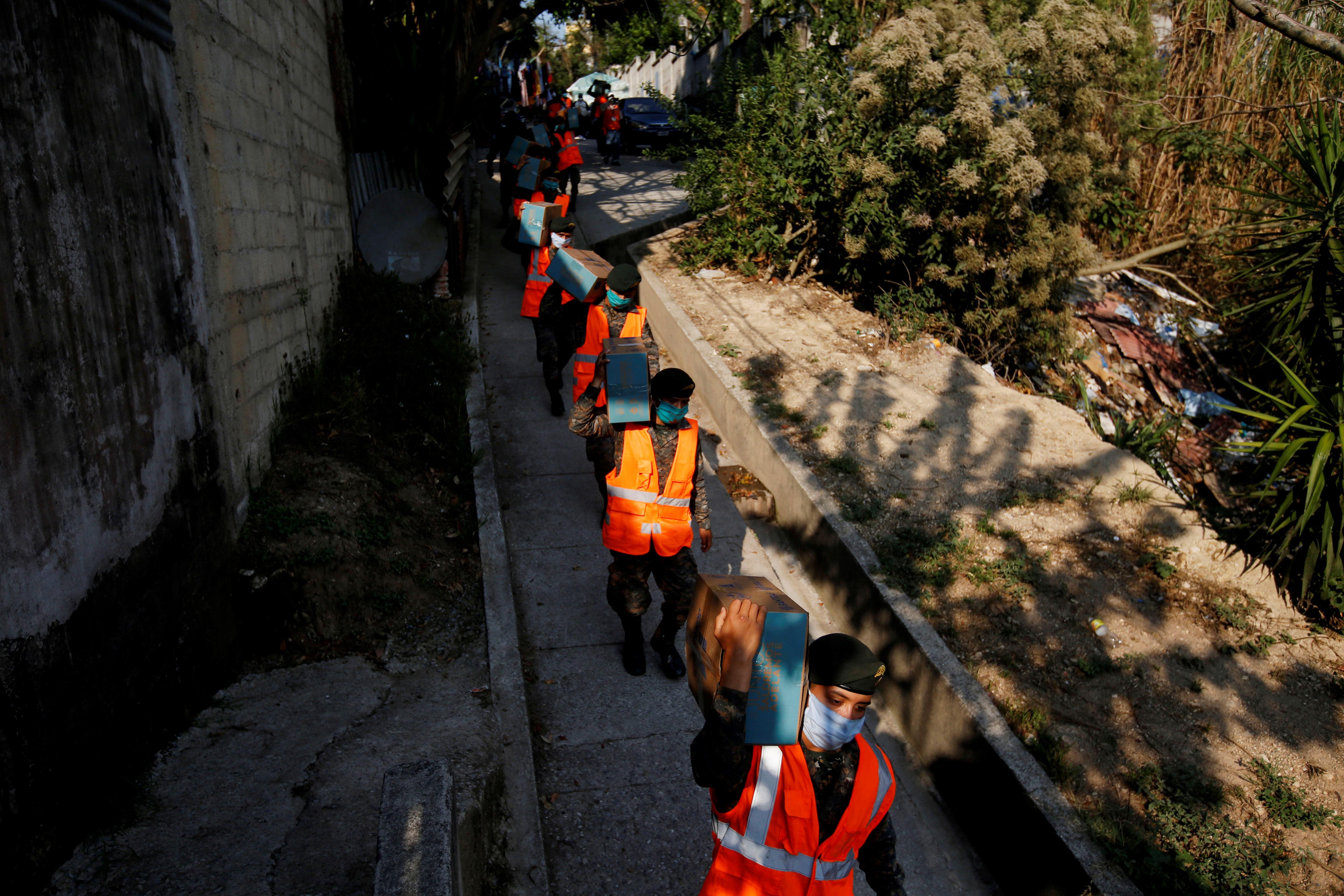 Soldados del Ejército de Guatemala y policías reparten cajas con comida básica en el asentamiento Santa Rosita, este lunes, en la capital. (Foto Prensa Libre: EFE)