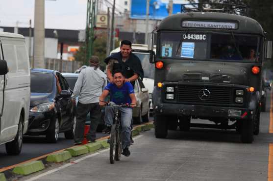 Dos jóvenes sonríen mientras avanzan en el carril del Transmetro seguidos de un vehículo que lleva personas a la zona 12 de Villa Nueva. Foto Prensa Libre: Óscar Rivas
