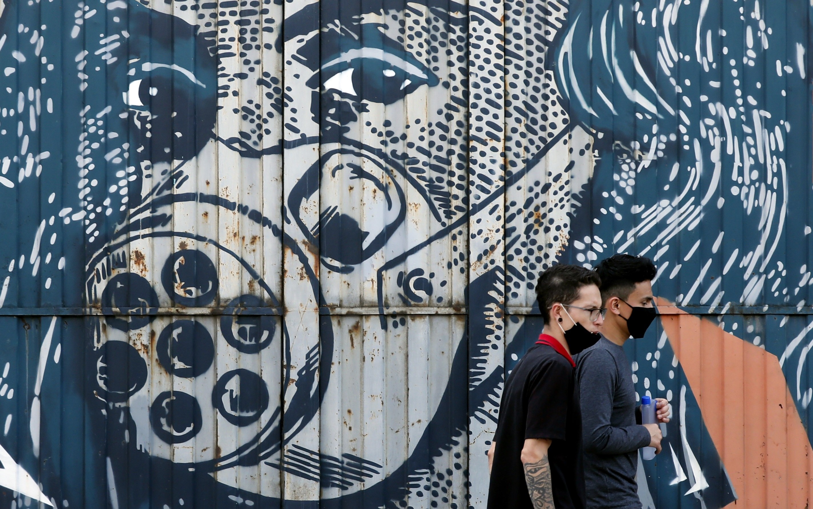 Personas usan tapabocas mientras pasan frente a un graffiti en la zona industrial, este miércoles en Bogotá, Colombia. (Foto Prensa Libre: EFE)