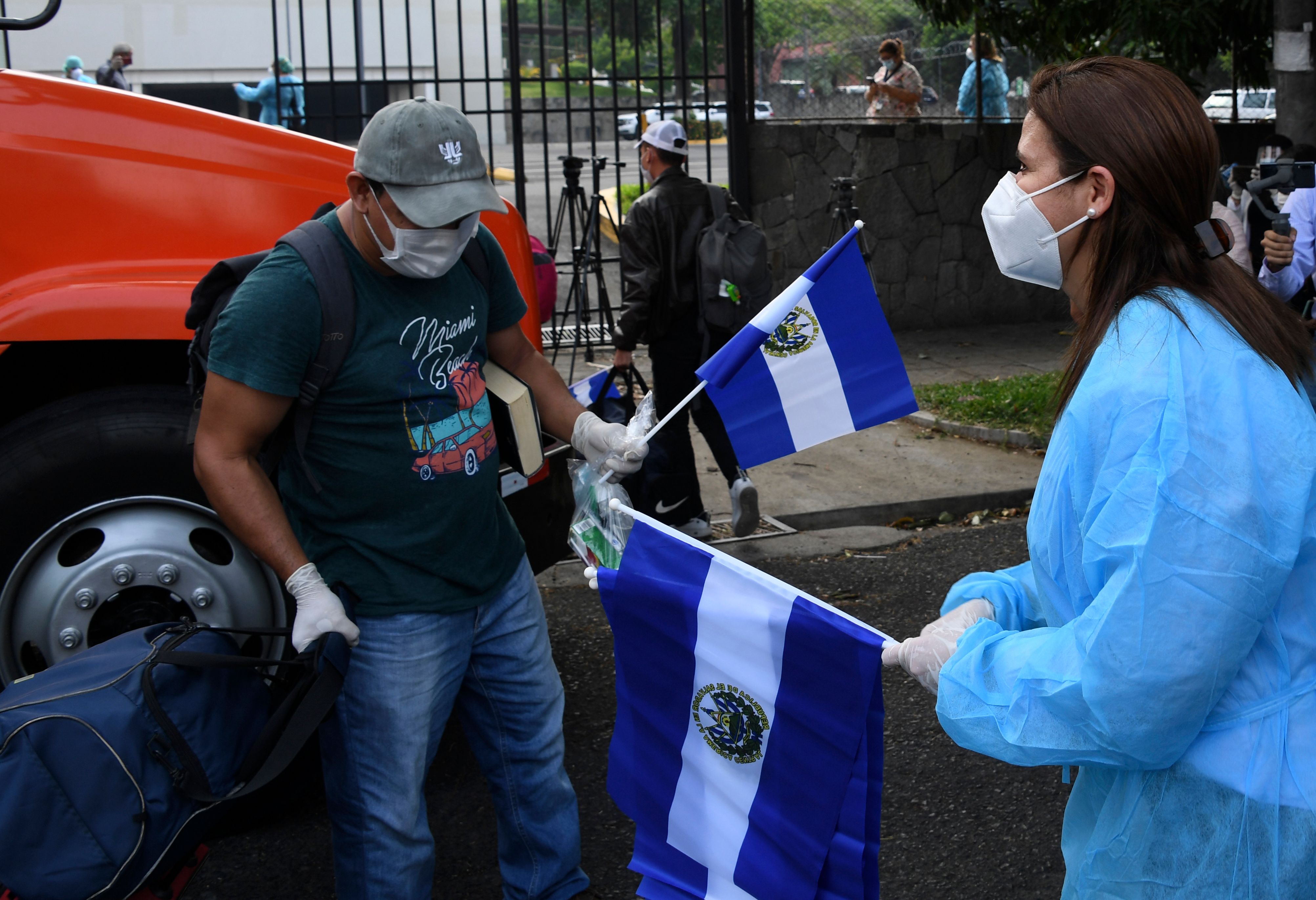 Una trabajadora sanitaria entrega una bandera a un salvadoreño que recién ingresa a un centro de cuarentena. (Foto Prensa Libre: AFP)