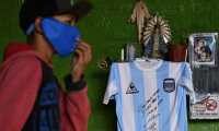 A kid walks pass a replica of Argentina's football team jersey used during the final of the FIFA World Cup Mexico '86, handwrited and signed by former football star Diego Maradona hangs from a catholic altar in a community kitchen during the lockdown imposed by the government against the spread of the new coronavirus, COVID-19, in Jose C. Paz, Buenos Aires, Argentina, on May 8, 2020. - Maradona's signed jersey will be raffled among those who donate food to feed people at a working class neighborhood called Rene Favaloro. (Photo by JUAN MABROMATA / AFP)