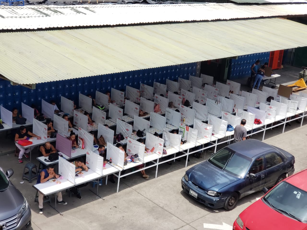 Empleados de una fábrica de textiles almuerzan en un área en que se instalaron separadores plásticos para evitar contacto y contagios de coronavirus. (Foto Prensa Libre: Cortesía) 