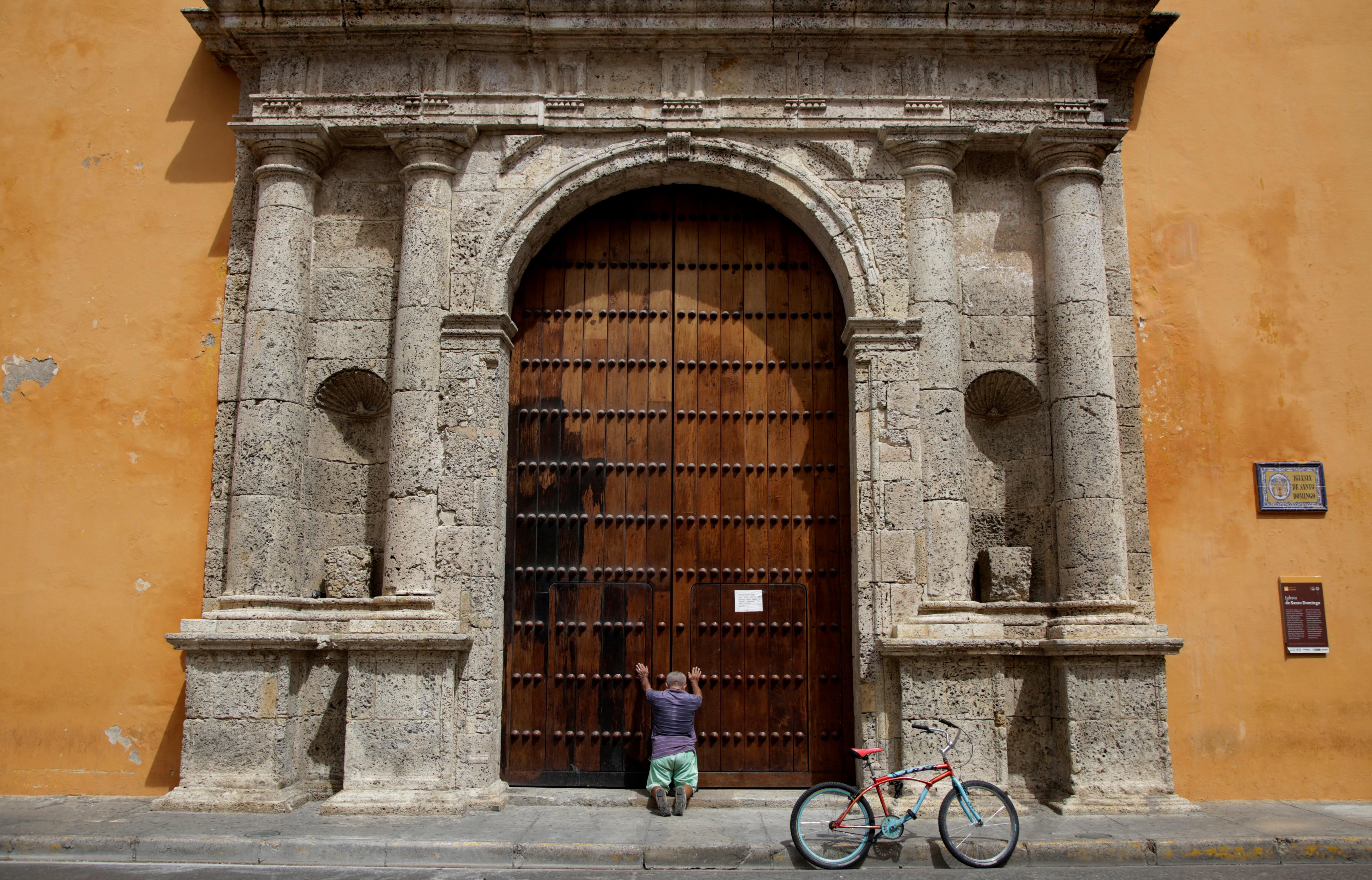 Fotografía del 1 de junio de 2020 que muestra a un hombre arrodillado ante las puertas de la iglesia de Santo Domingo de Cartagena (Colombia). (Foto Prensa Libre: EFE)