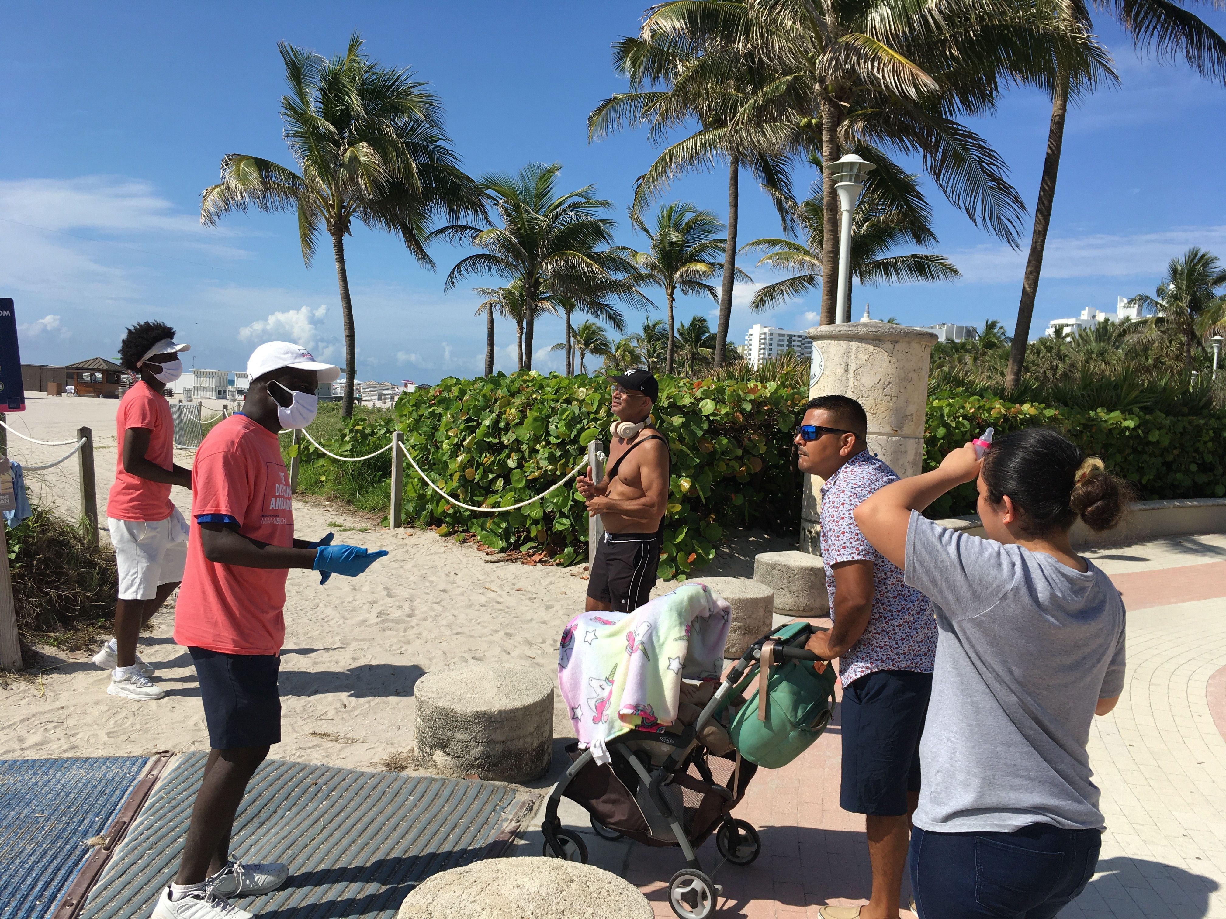 Unos jóvenes revisan las máscaras de unas personas a su llegada a la playa de Miami Beach, Florida, el 10 de junio de 2020. (Foto Prensa Libre: EFE).