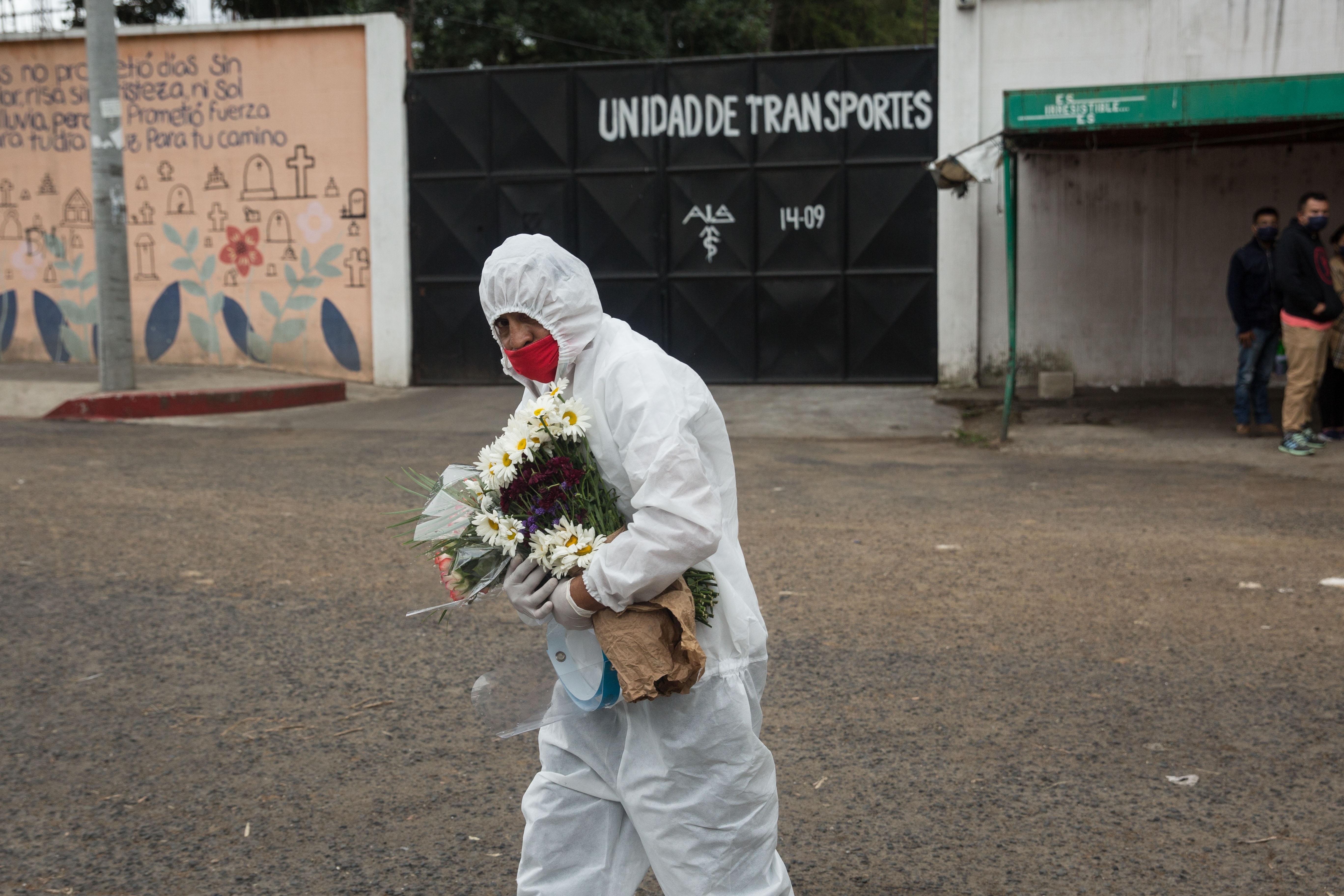 Un trabajador de Salud traslada flores que parientes de un fallecido por covid-19 llevaron al cementerio La Verbena, que fue designado para sepultar a las víctimas de la pandemia. (Foto Prensa Libre: EFE)