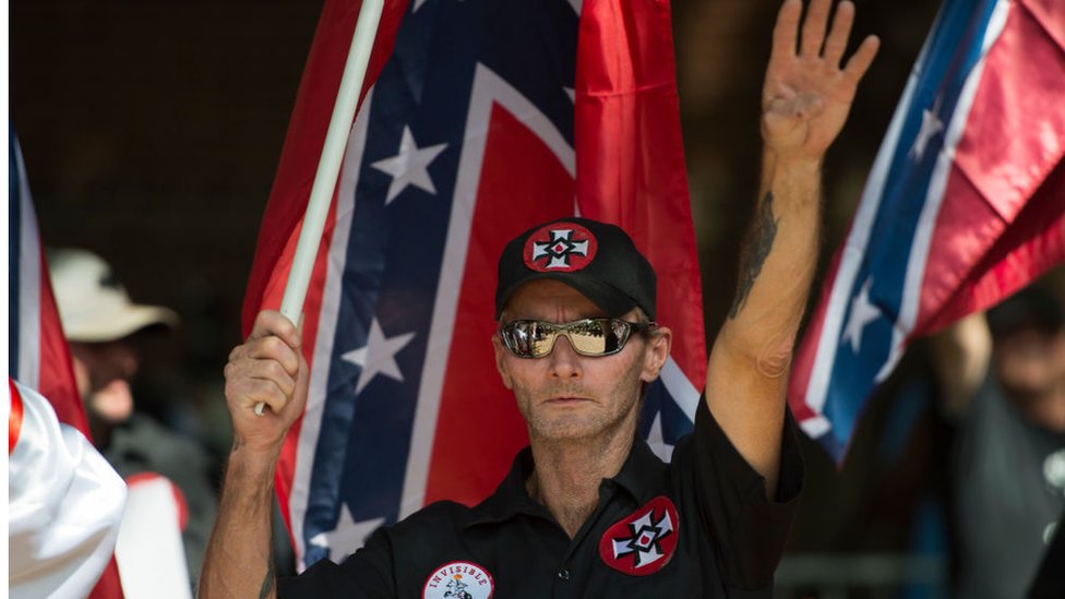 Un supremacista hace el saludo nazi con una bandera de la confederación y las cruces símbolo del Ku Klux Klan. (Foto Prensa Libre: Getty Images)