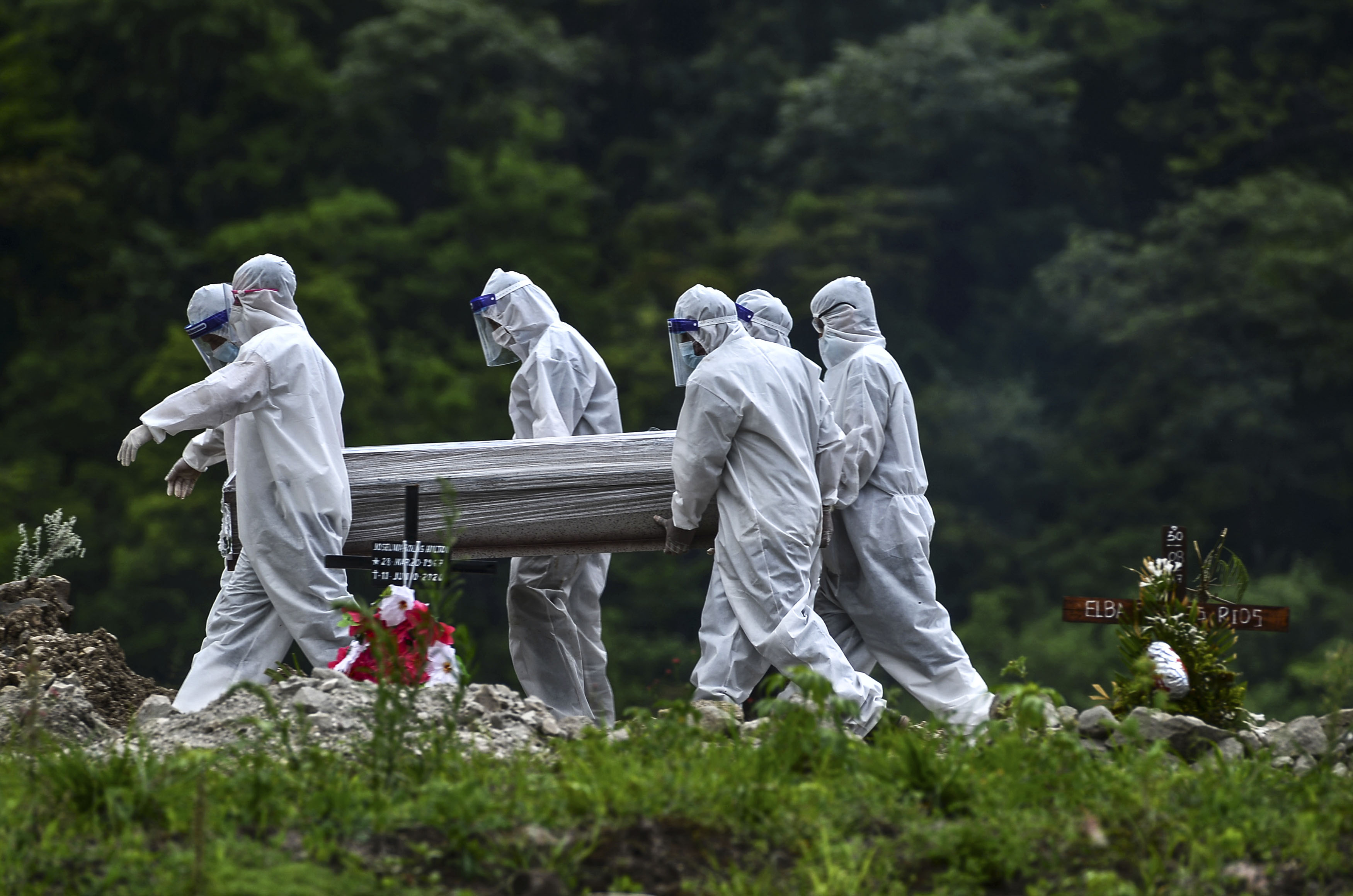 Varios hombres con trajes protectores llevan el cuerpo de una víctima de covid-19. (Foto Prensa Libre: AFP)