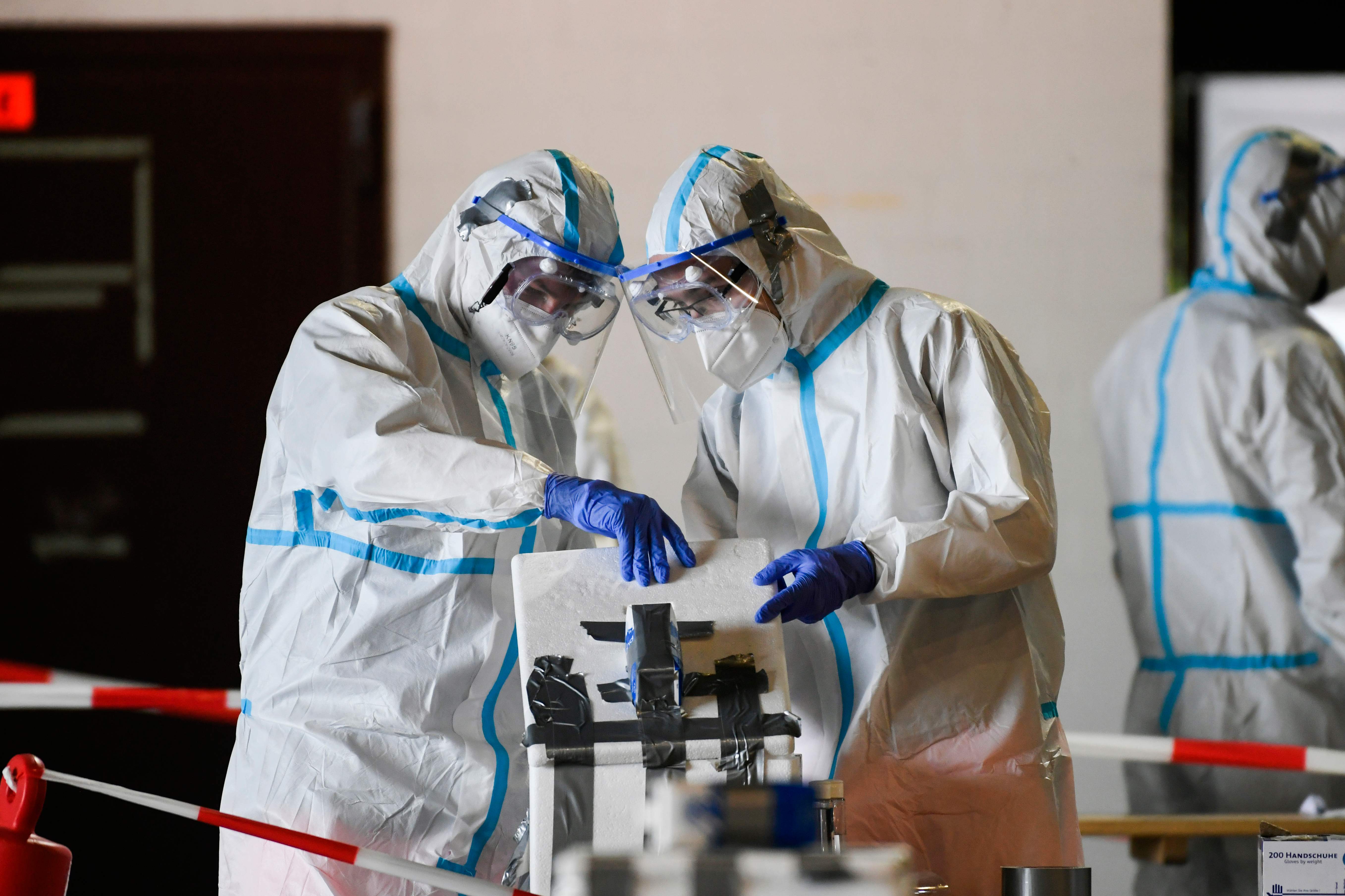 Helpers in protective suits prepare to take samples to test people in their vehicle at a coronavirus testing station set up at the former Guetersloh military airport on June 30, 2020. - German Armed Forces and aid organizations have set up a smear station, where people can be tested for Covid-19 after the coronary outbreak at the Toennies meat plant. (Photo by Ina FASSBENDER / AFP)