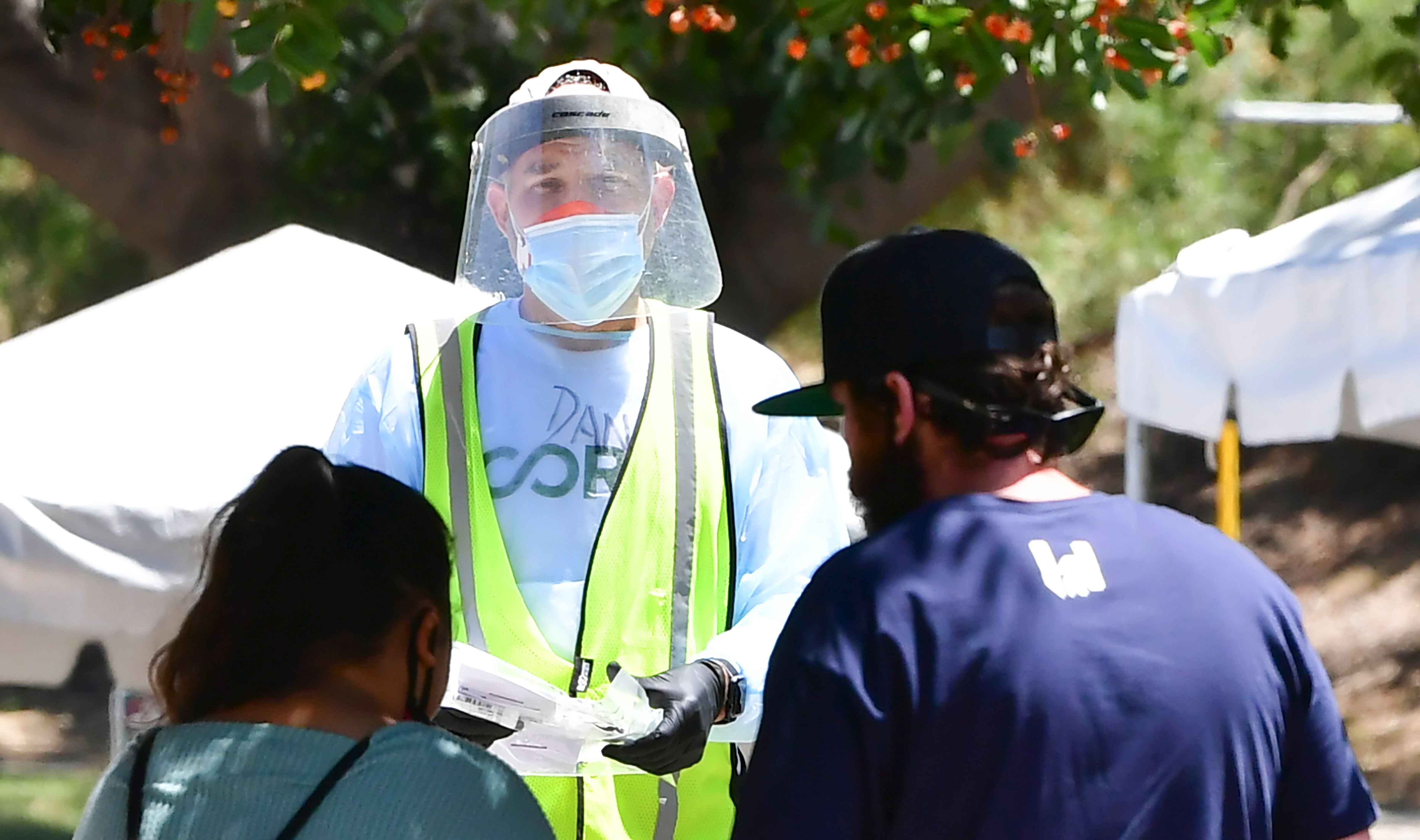 Un voluntario vestido con protección completa ofrece kits de prueba a las personas en un sitio de prueba covid-19 sin cita previa, en Los Ángeles, California. (Foto Prensa Libre: AFP)
