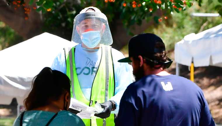 Un voluntario vestido con protección completa ofrece kits de prueba a las personas en un sitio de prueba covid-19 sin cita previa, en Los Ángeles, California. (Foto Prensa Libre: AFP)