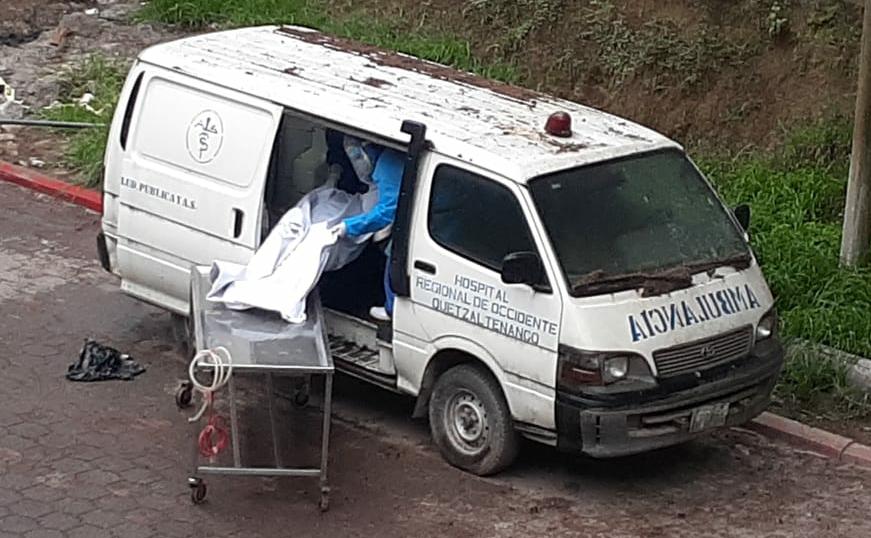 Empleados del Hospital Regional de Occidente ingresan el cadáver de una víctima de covid-19 a una vieja ambulancia que sirve como morgue. (Foto Prensa Libre: Raúl Juárez)