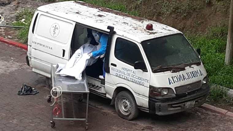 Empleados del Hospital Regional de Occidente ingresan el cadáver de una víctima de covid-19 a una vieja ambulancia que sirve como morgue. (Foto Prensa Libre: Raúl Juárez)