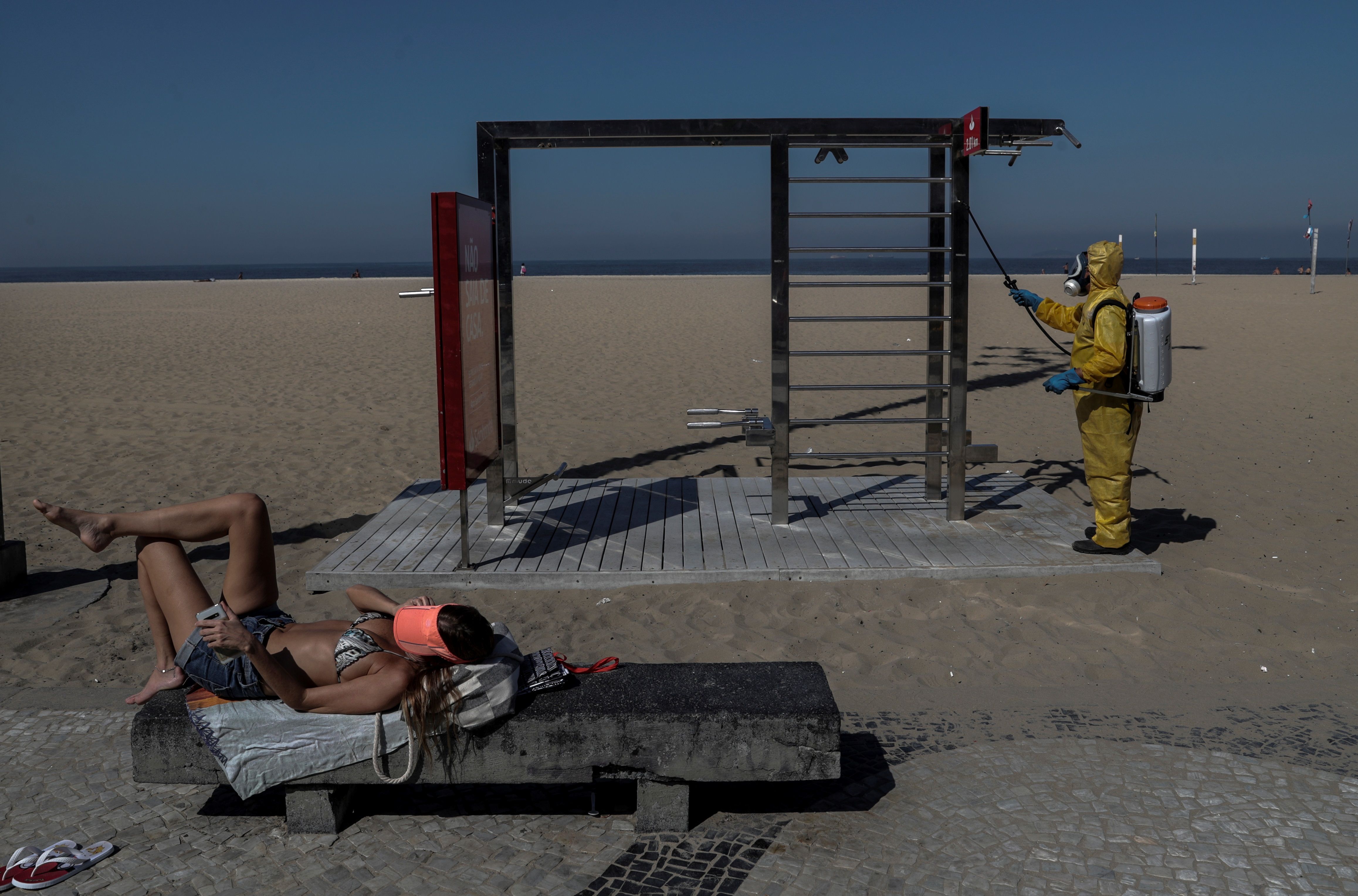 Una mujer toma el sol, mientras un hombre limpia la zona de ejercicio de la playa de Copacabana, en Río de Janeiro (Brasil), en la reapertura económica a inicios de junio de 2020. (Foto Prensa Libre: EFE)