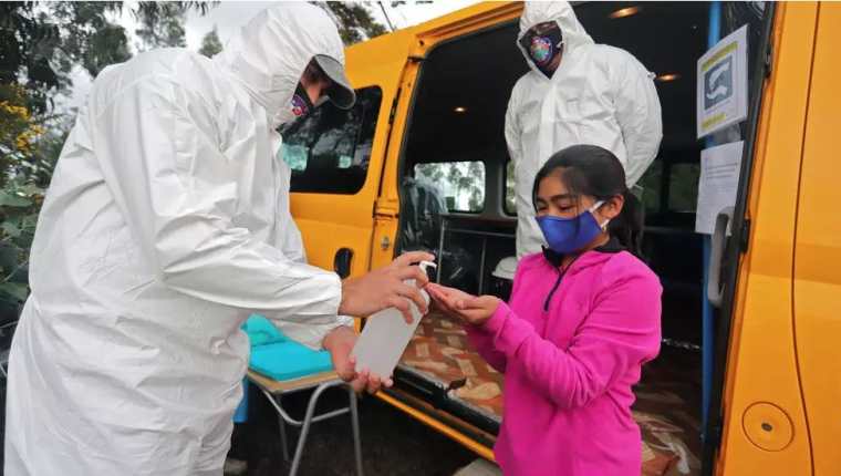 Una niña recibe alcohol en gel para recibir clases en la furgoneta. (Foto Prensa Libre: AFP)