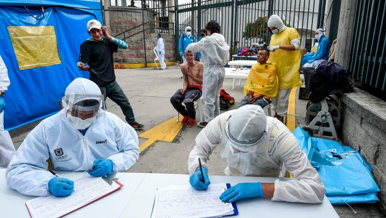 Workers of Bogota's Municipality wearing personal protective equipment against the spread of the new coronavirus, assist homeless people in Bogota, on May 20, 2020. - Colombia will extend the isolation measures taken against the pandemic until May 31, after which it will begin a gradual process of economic reactivation, President Ivan Duque announced Tuesday. (Photo by Juan BARRETO / AFP)
