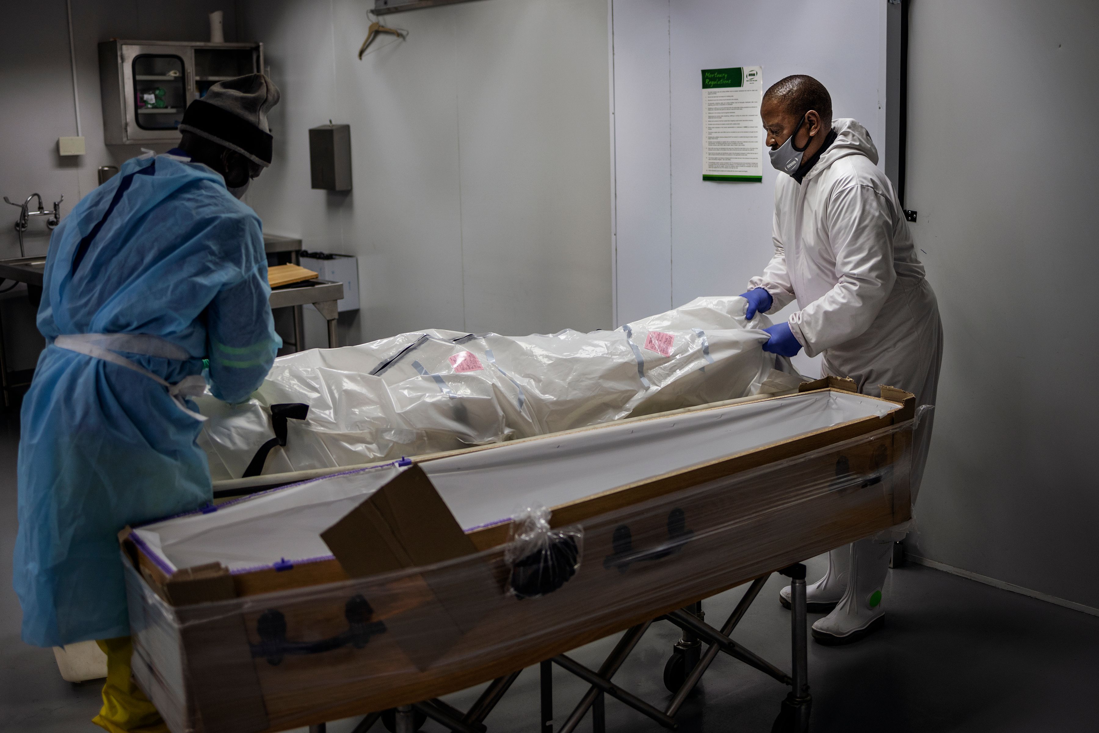 Undertakers move the remains of a COVID-19 coronavirus patient into a coffin at the AVBOB funeral house in Soweto, on July 24, 2020. (Photo by Michele Spatari / AFP)