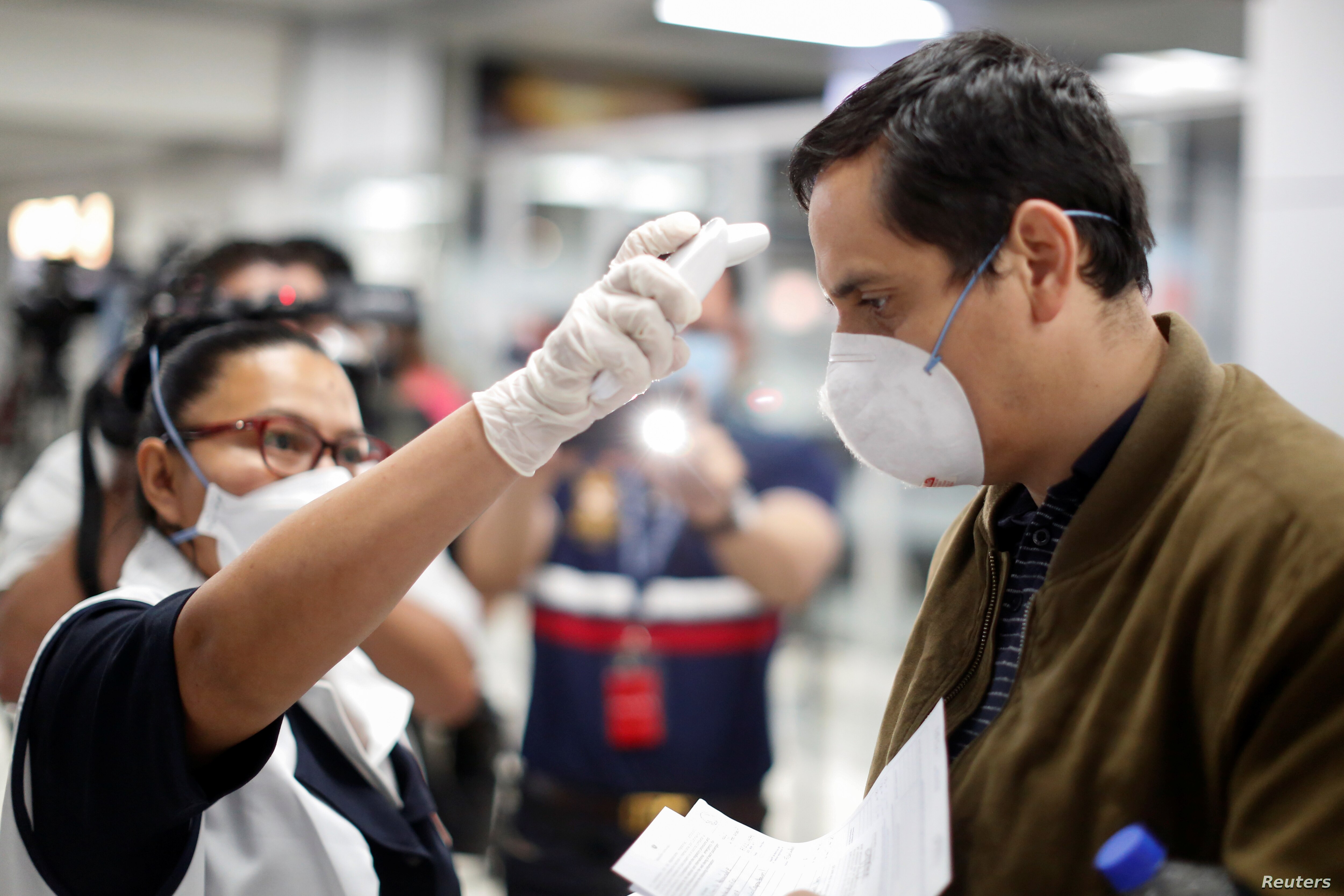 Un pasajero es revisado con un escáner térmico por un trabajador de salud pública en el aeropuerto internacional Óscar Romero y Galdamez, en El Salvador, el 12 de marzo de 2020.