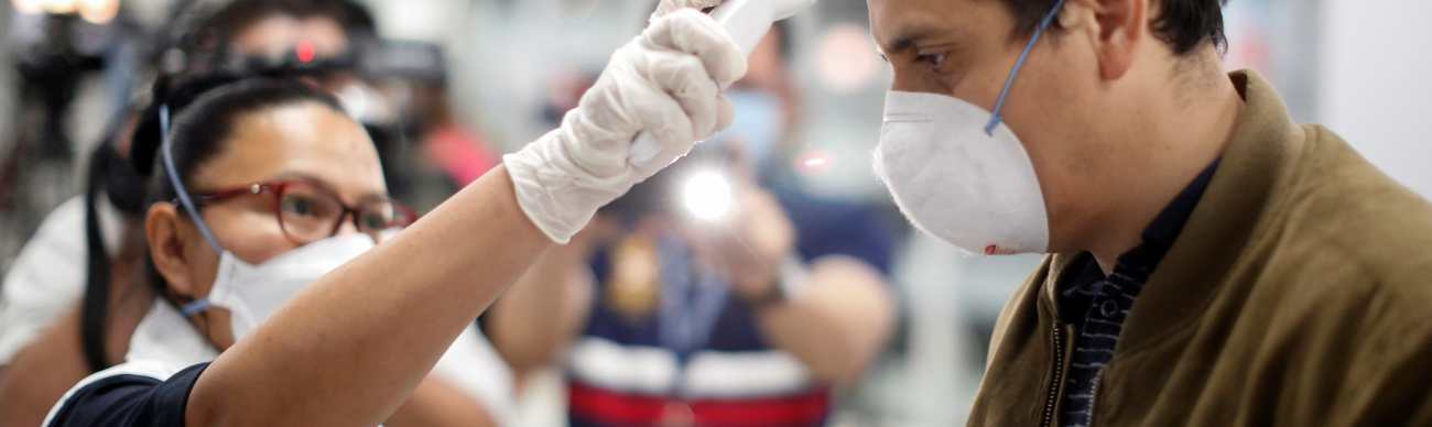 Un pasajero es revisado con un escáner térmico por un trabajador de salud pública en el aeropuerto internacional Óscar Romero y Galdamez, en El Salvador, el 12 de marzo de 2020.