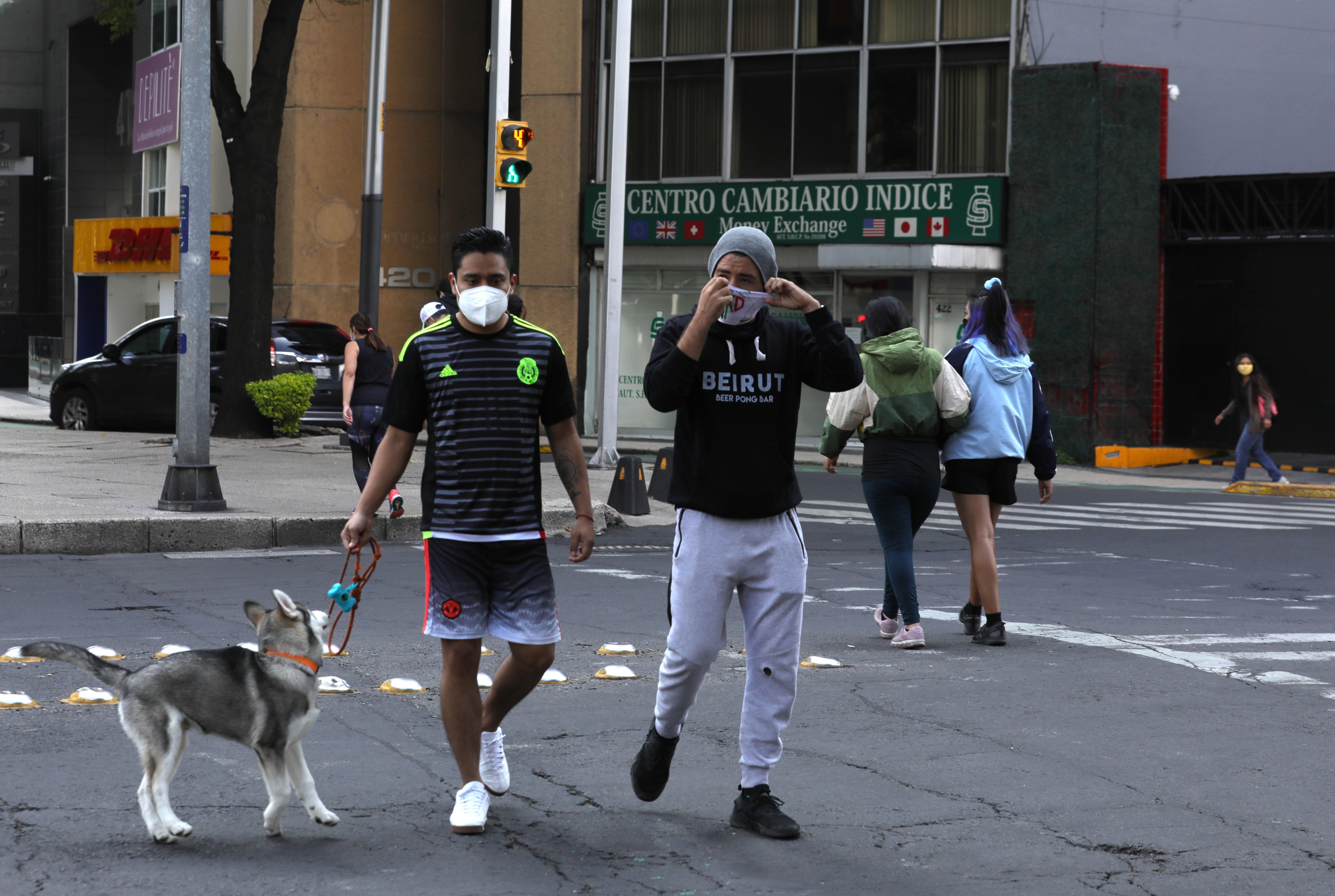 Dos hombres usan mascarilla, mientras pasean con su perro en una calle de la ciudad de México. (Foto Prensa Libre: EFE)