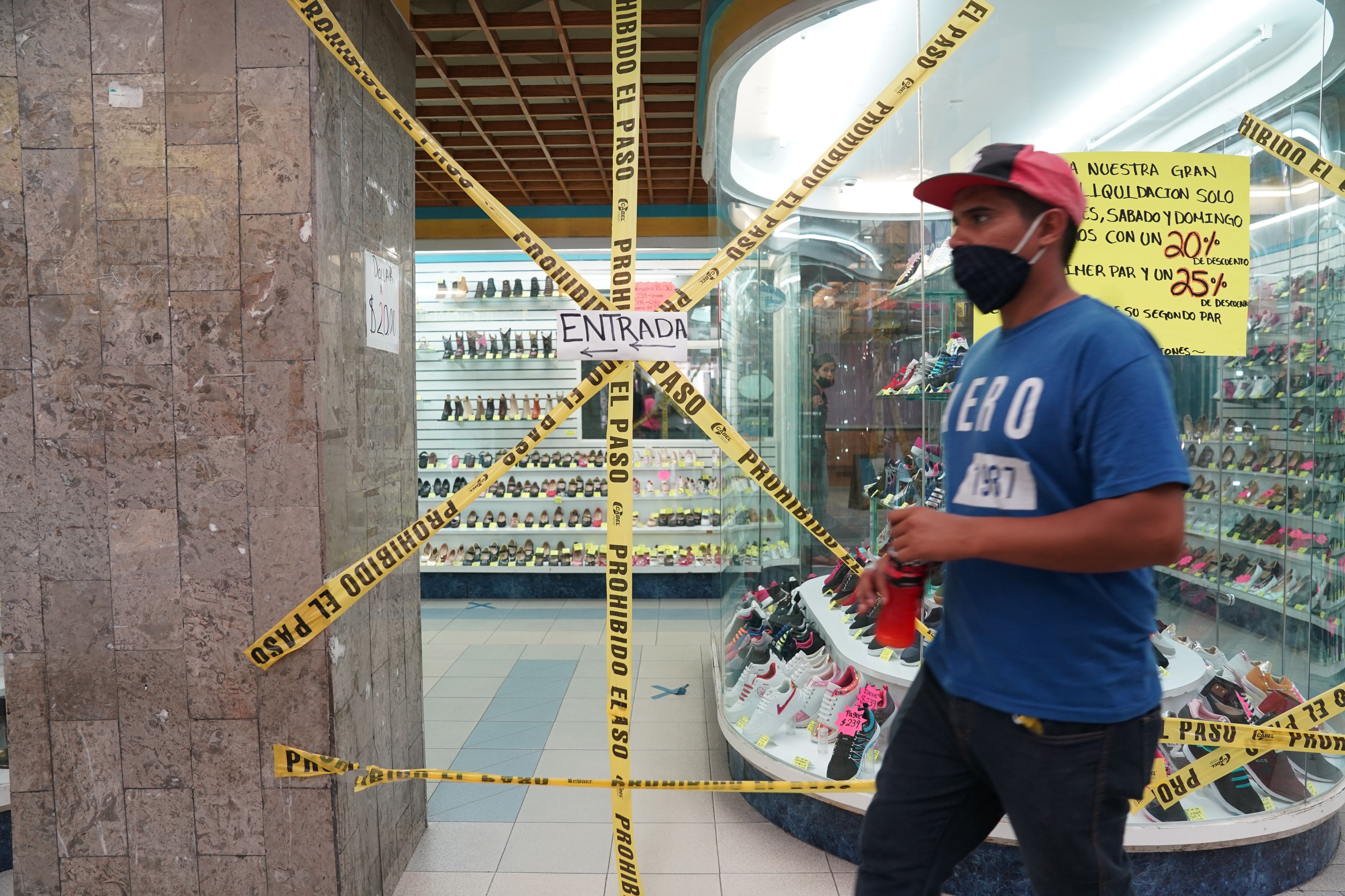 A man stands next to caution tape that prohibits entry to a shoe store during the COVID-19 pandemic in Ciudad Juarez, Mexico on August 2, 2020. (Photo by Bryan R. Smith / AFP)