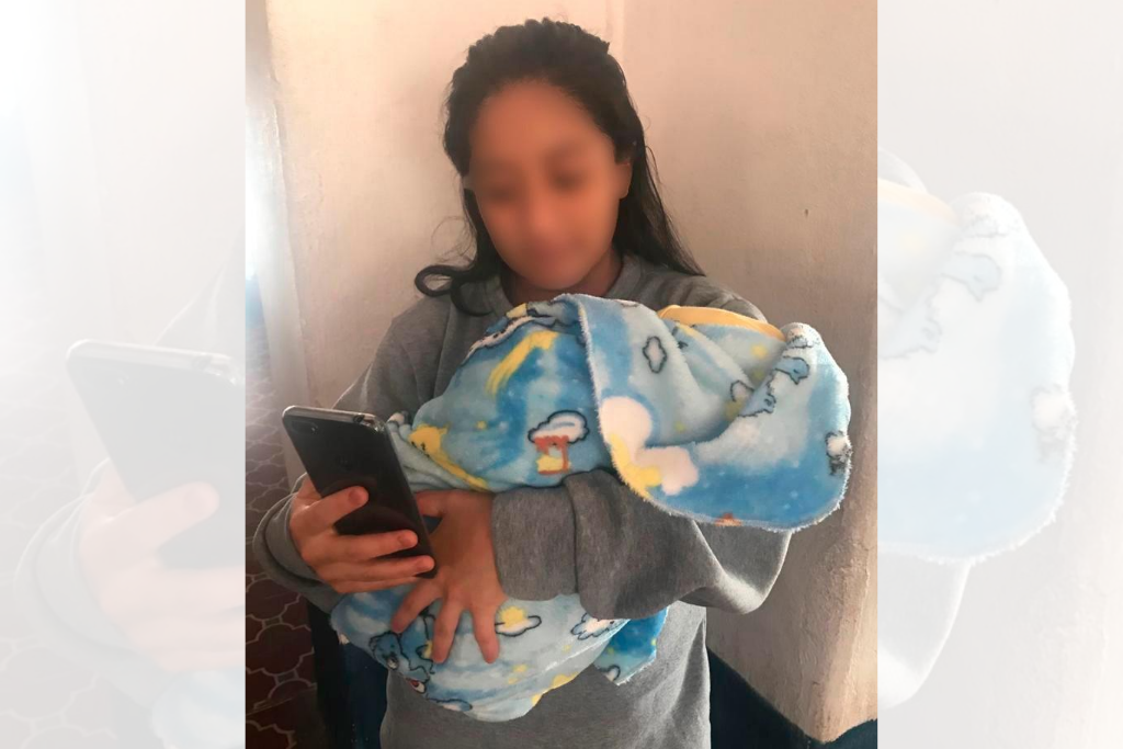 Una menor carga a su bebé mientras se comunica con su familia a través de un teléfono móvil habilitado por la SBS durante la pandemia.