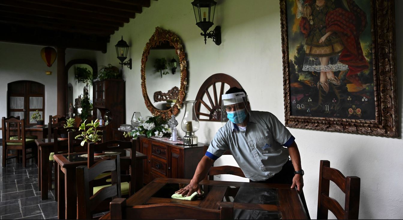 Un empleado limpia una mesa en el área de restaurante de un hotel en Antigua Guatemala que comenzó la reapertura en medio de la pandemia. (Foto Prensa Libre: AFP)