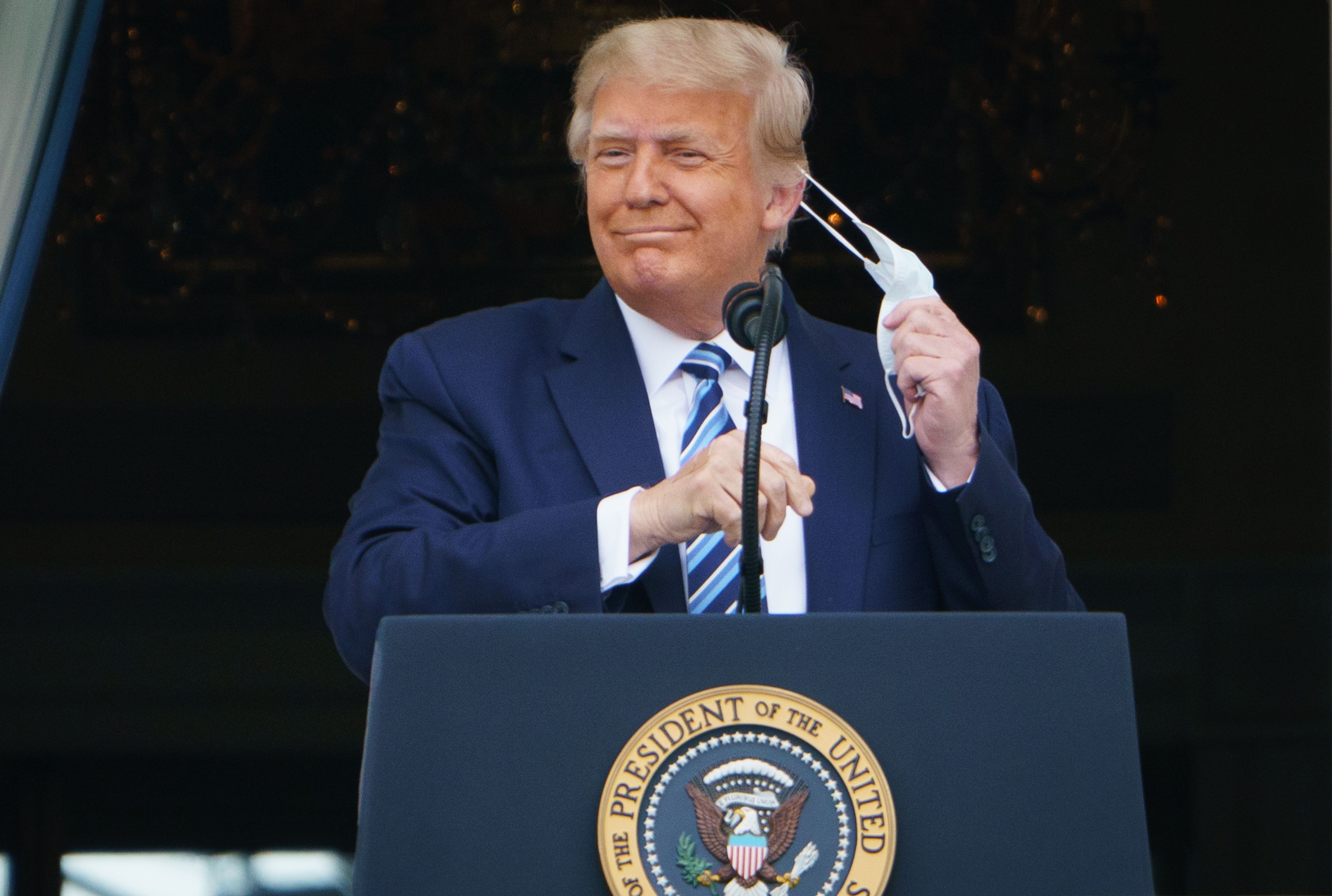El presidente Donald Trump se quita la mascarilla antes de hablar desde el pórtico sur de la Casa Blanca en Washington DC, durante un mitin.  (Foto Prensa Libre: AFP)