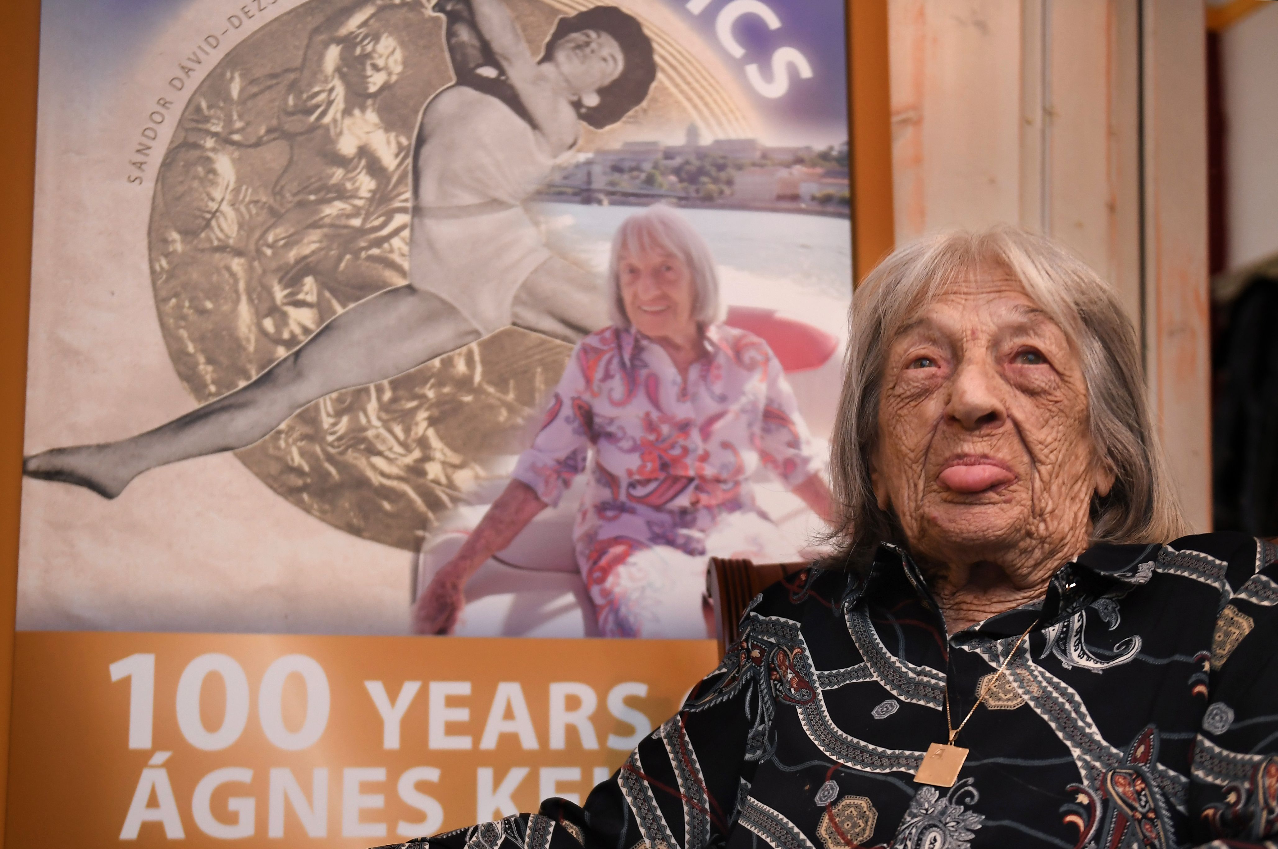 La campeona retirada de gimnasia artística de origen húngaro israelí, Ágnes Keleti, posa frente a un poster sobre su biografía en Budapest. Ella cumple 100 años y es la campeona olímpica con más edad en estar viva. (Foto Prensa Libre: AFP)