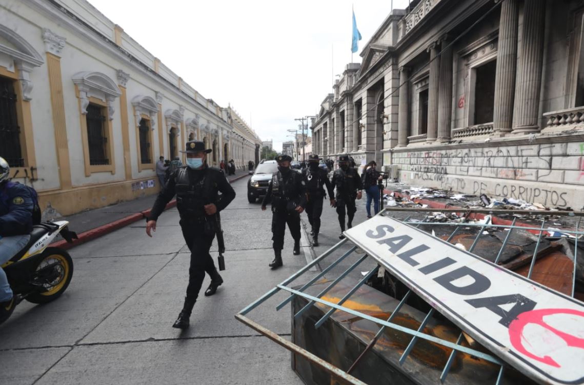 Policías avanzan frente al Congreso, en donde se pude observar parte de los daños causados en la protesta del 21 de noviembre.  (Foto Prensa Libre: Érick Ávila)