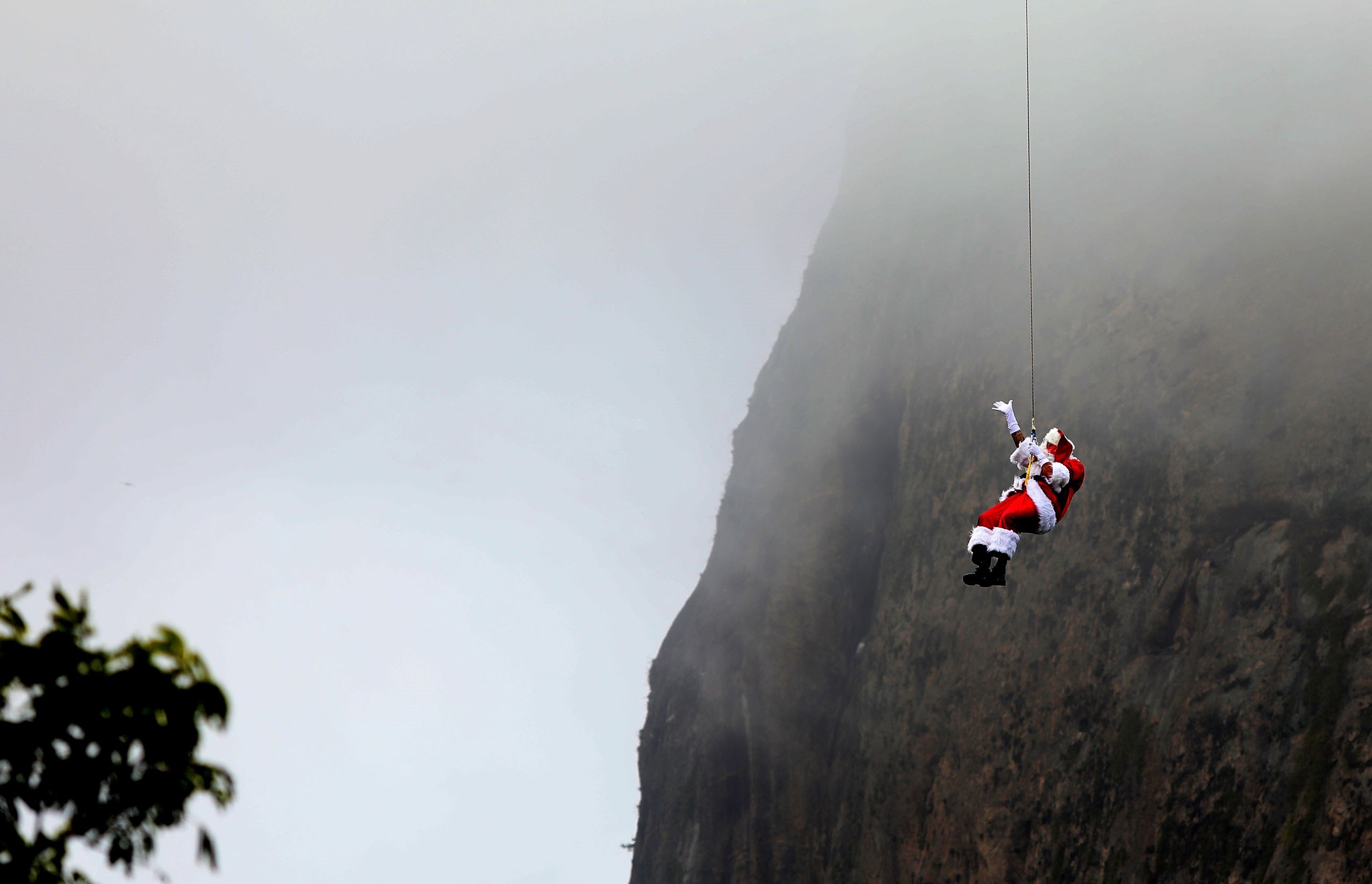 Santa Claus hizo la travesía entre los dos cerros que conforman el Pan de Azúcar, colgado en la parte externa de un teleférico. (Foto Prensa Libre: EFE)